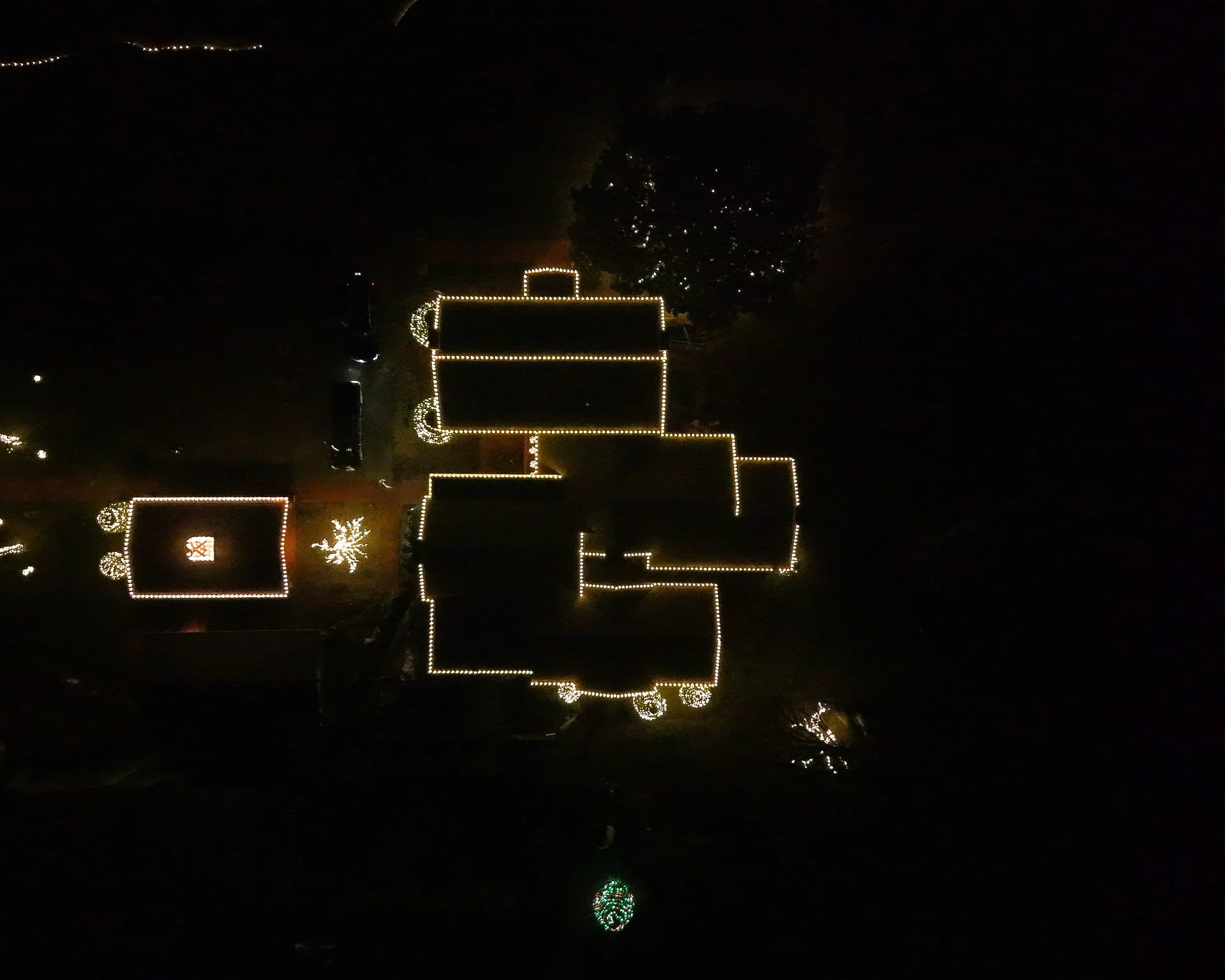 House outlined with Christmas lights at night, with trees decorated with lights nearby.