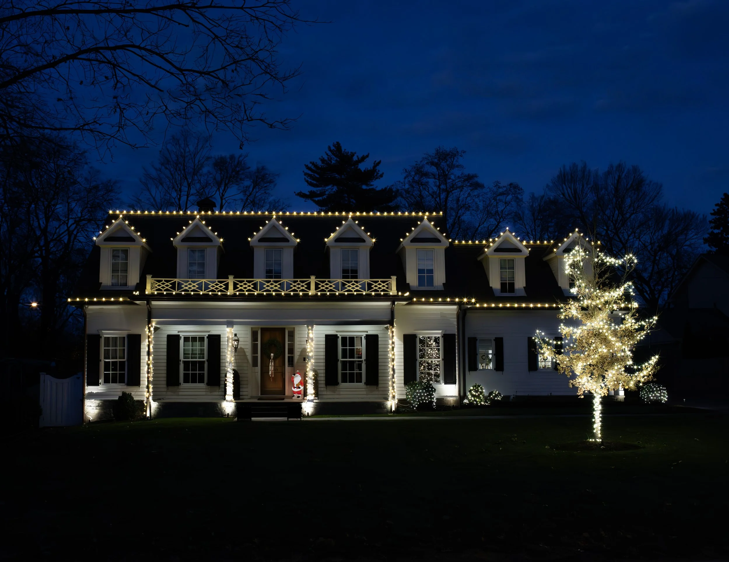 A house decorated with Christmas lights, including a lit tree in front, at night.