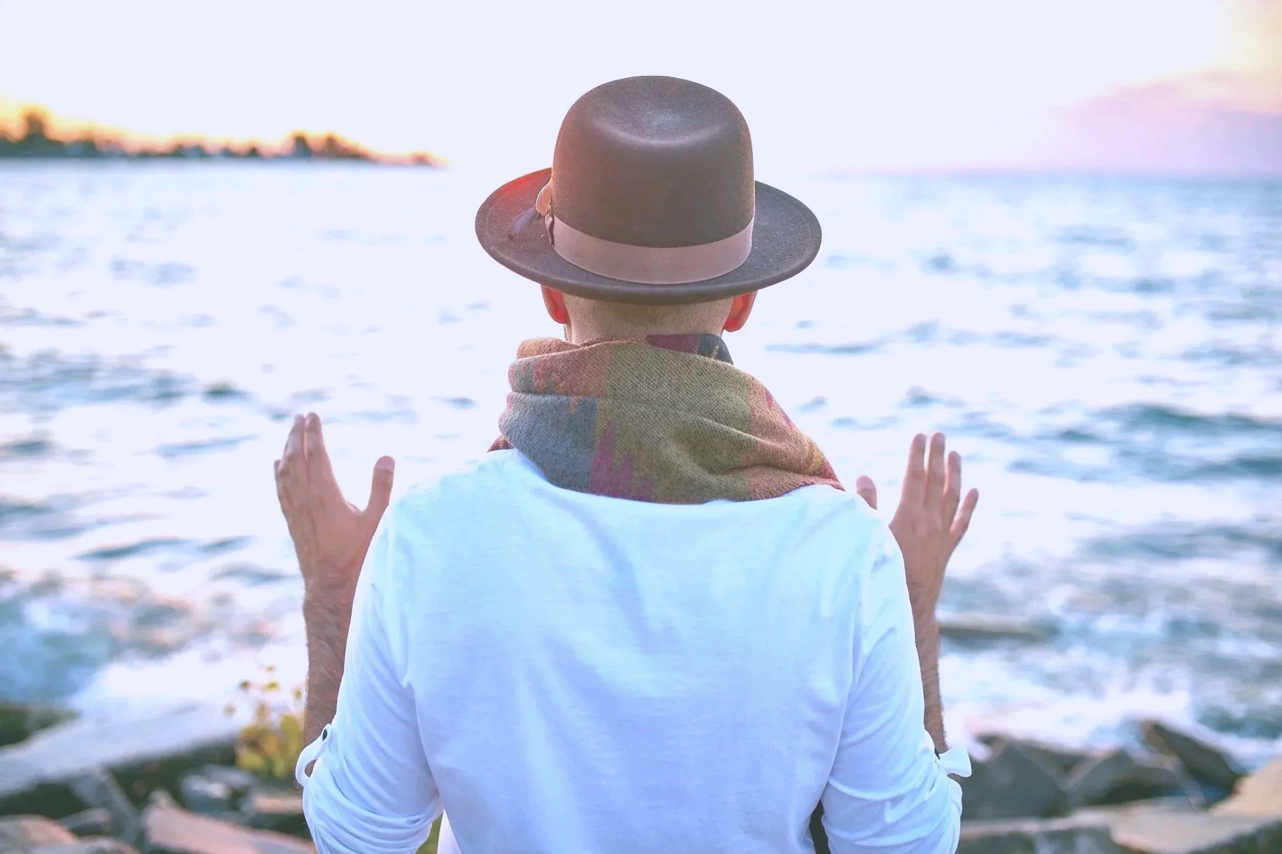 Man standing with hand up meditating by the ocean