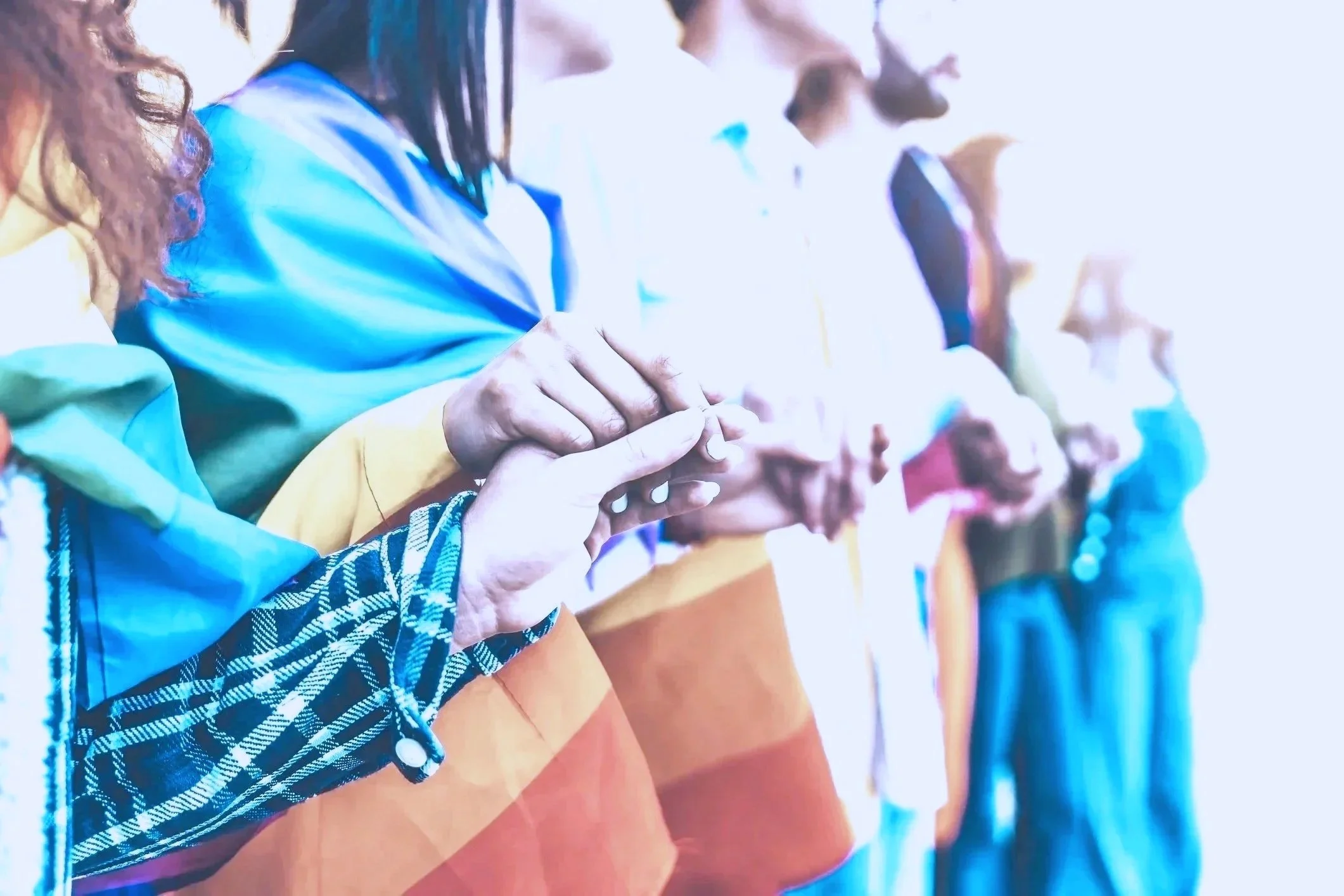 Diverse LGBTQ+ group holding hands with pride flag outdoors