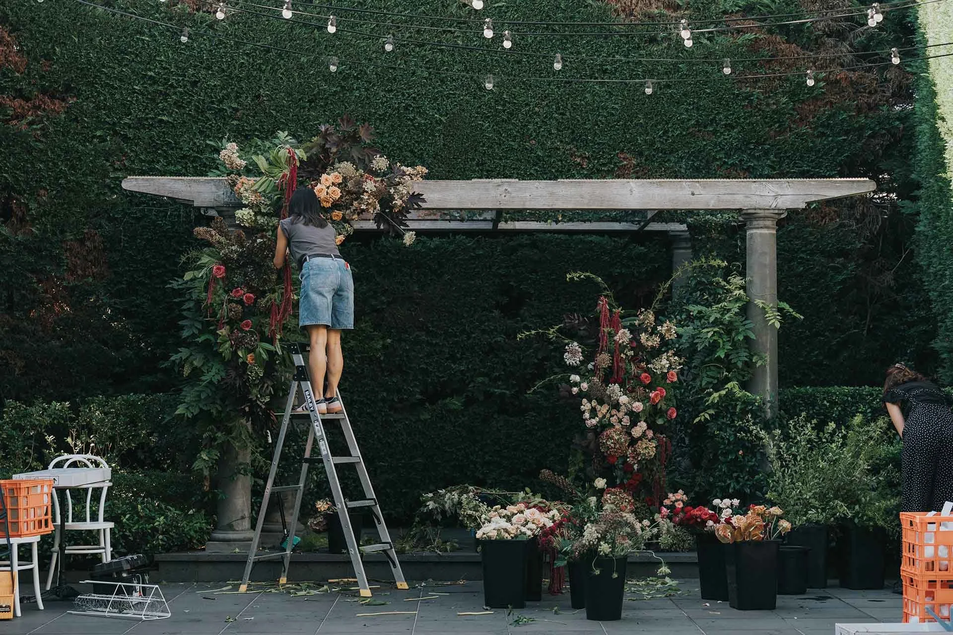 Florist installing large scale floral arrangement with ladder at wedding venue