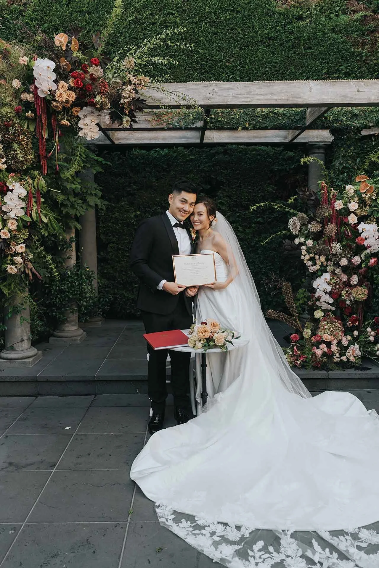 Couple signing wedding certificate under floral installation