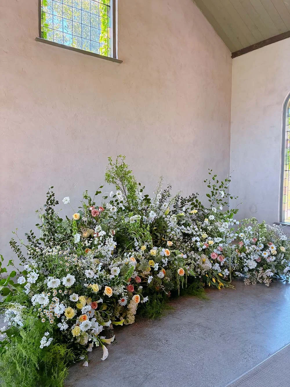 Ceremony floral meadow installation with seasonal white and soft pastel flowers indoors