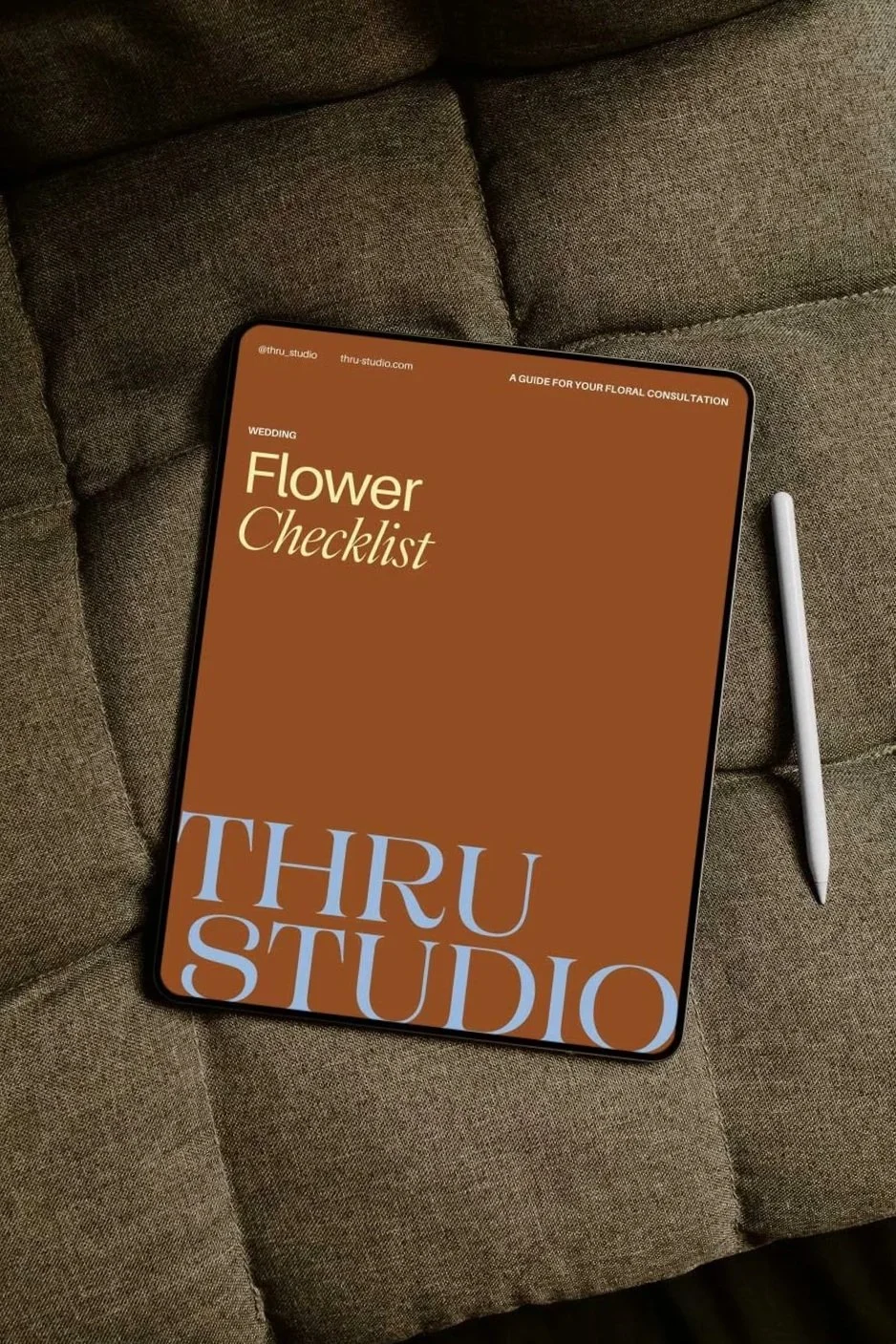 A tablet displays a flower checklist for wedding floral consultation on a brown background, placed on a grey fabric surface, accompanied by a white stylus pen.