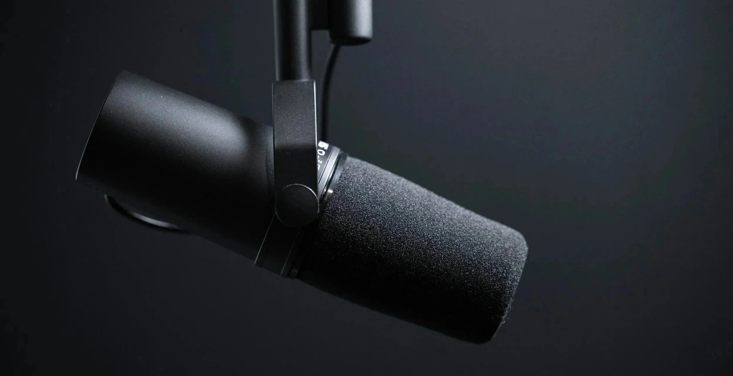 Close-up of a professional black studio microphone with foam windscreen against a dark background.