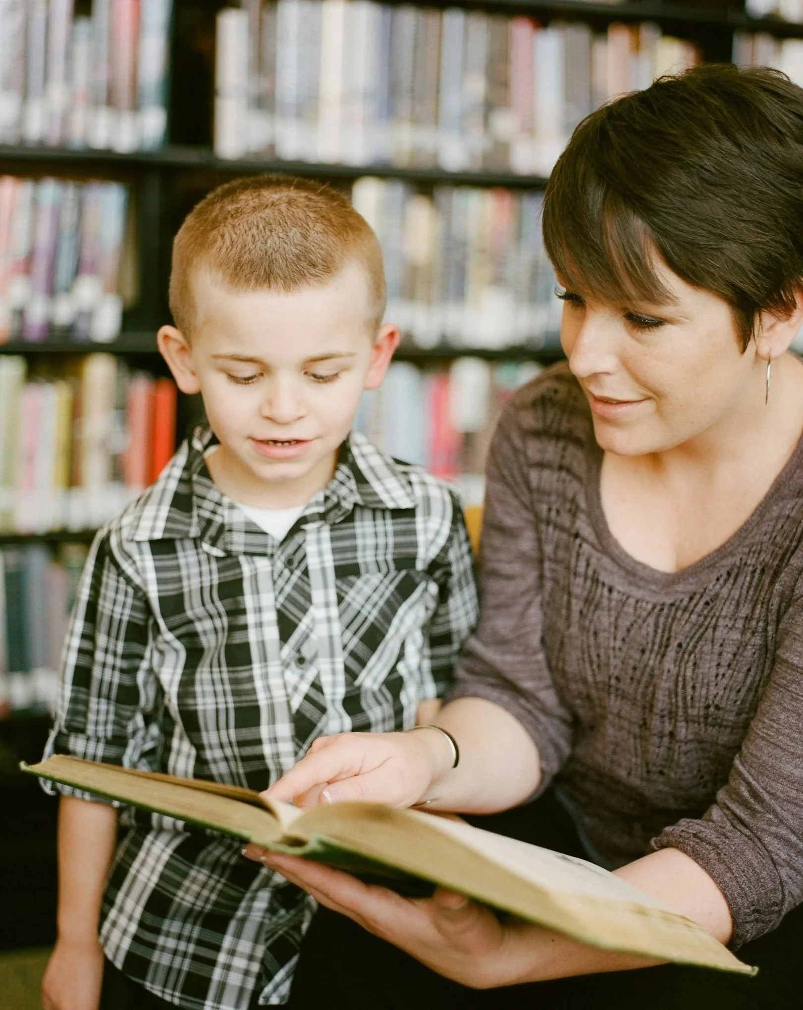 A woman and a young boy looking at a book together in a library.