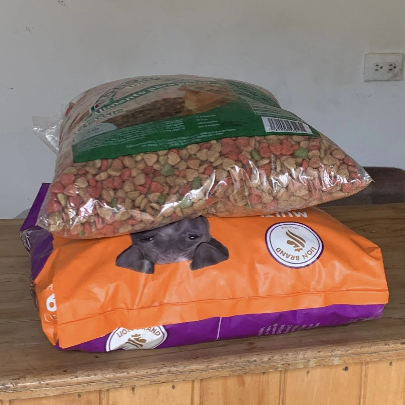 A bag of dog food with a picture of a dog's face on it, placed on a wooden surface, with a container of dry pet food on top.
