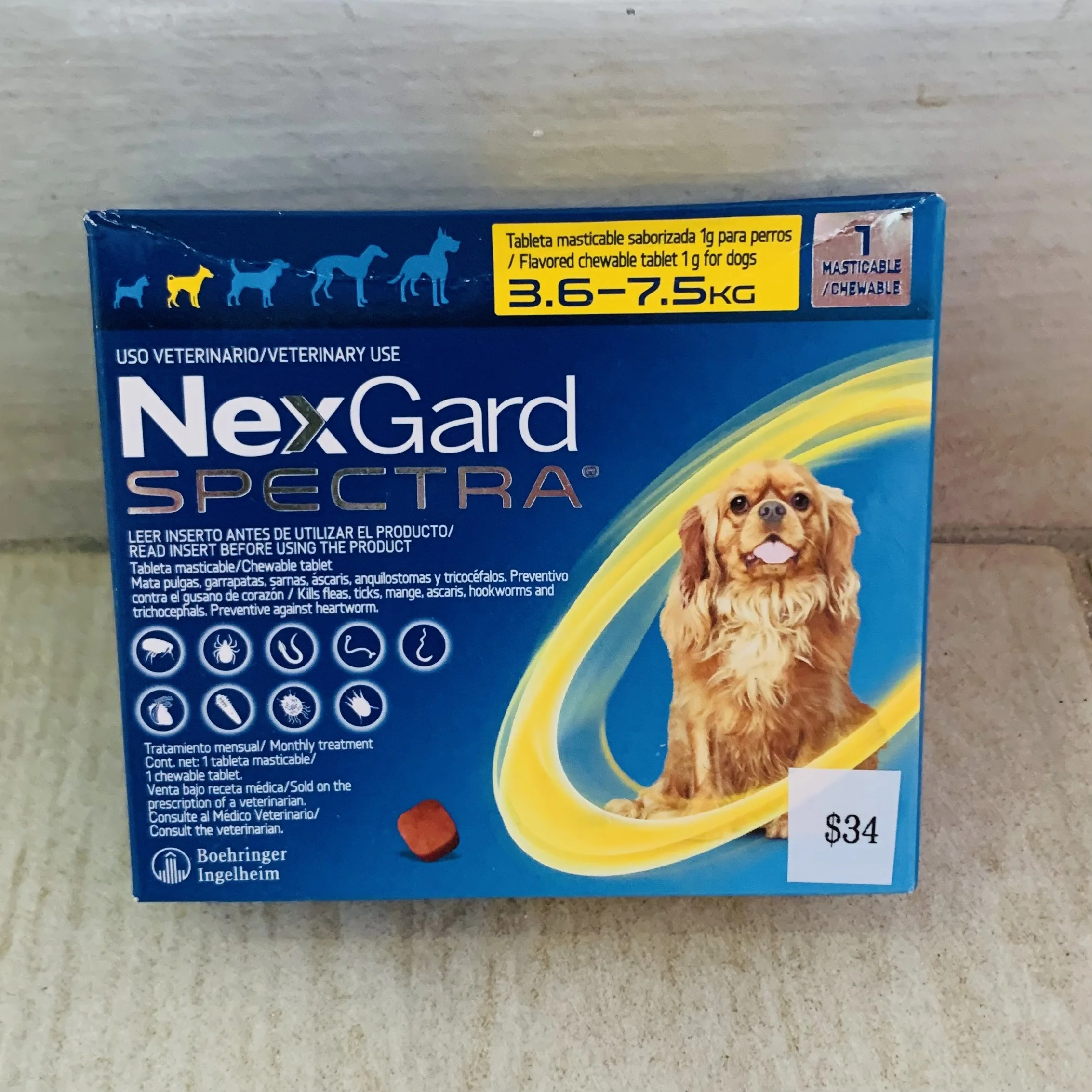 Blue box of NexGard Spectra chewable tablets with a picture of a dog on the front, yellow label indicating flavored chewable tablet for dogs weighing 3.6 to 7.5 kilograms, and a price tag of 34 dollars.