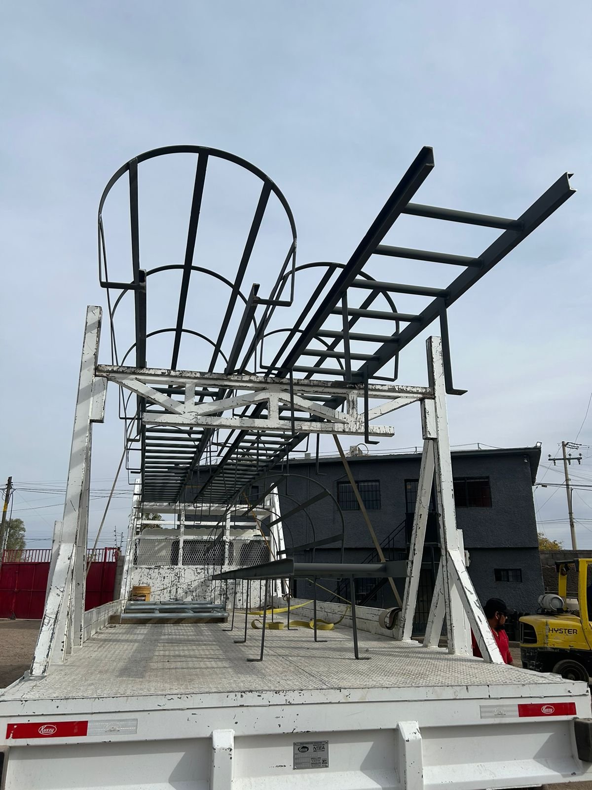 Metal framework structure on a flatbed truck, with a cloudy sky in the background.