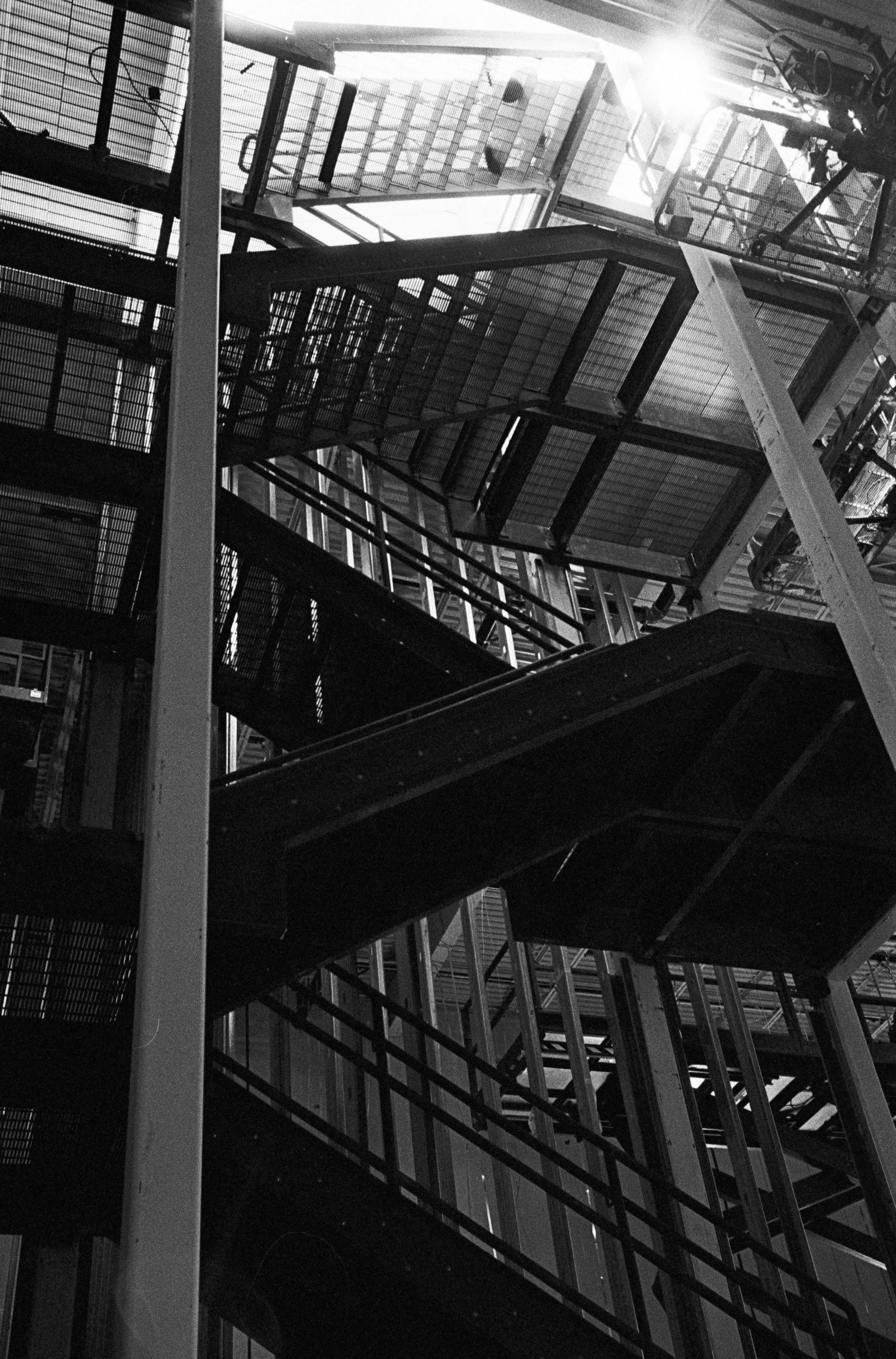 View from below of metal fire escape staircase with multiple levels and railings in a high-rise building, sunlight shining through the top.