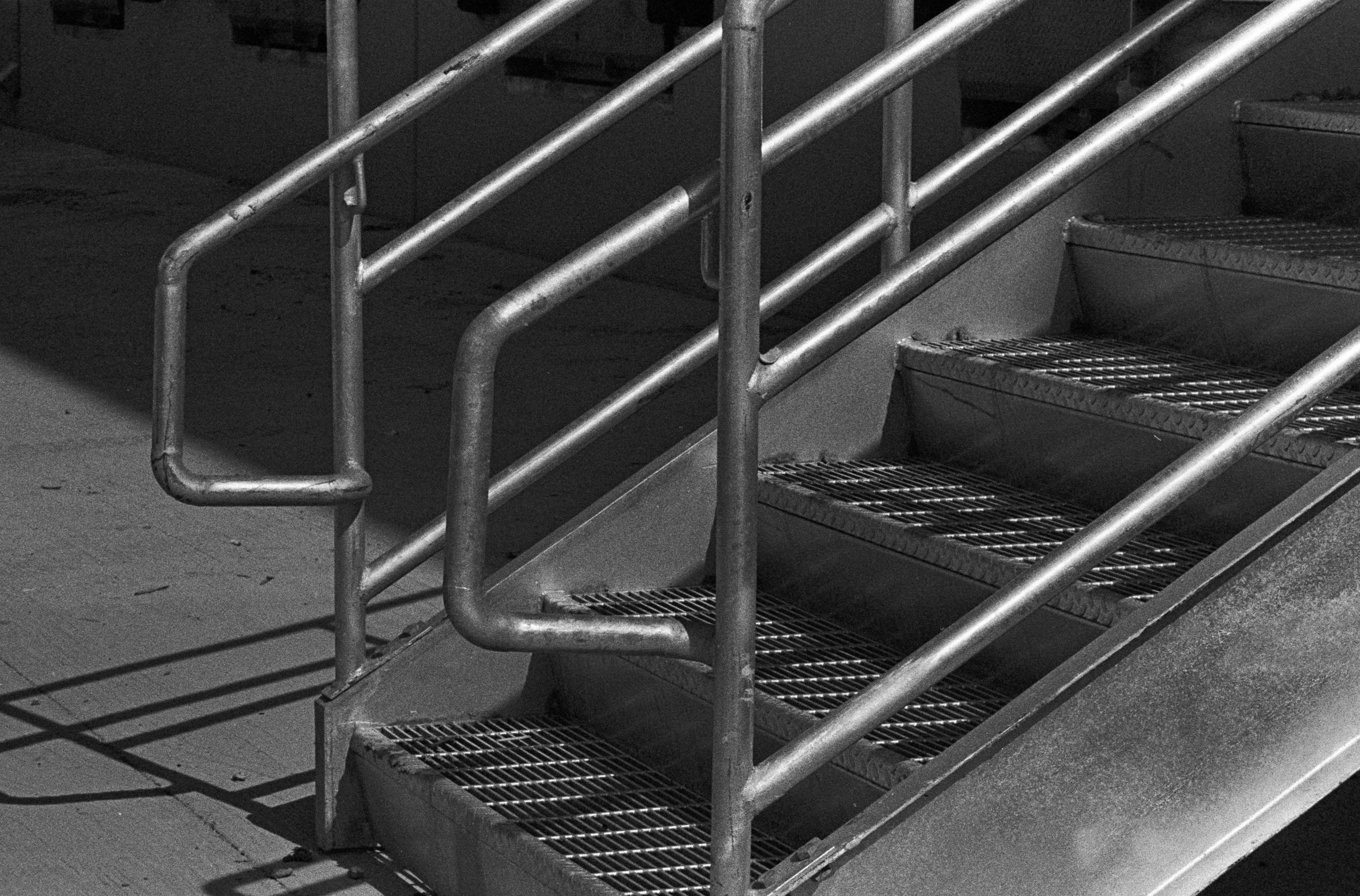 Metal stairs with handrails on both sides, leading upward, with shadows cast on the ground.