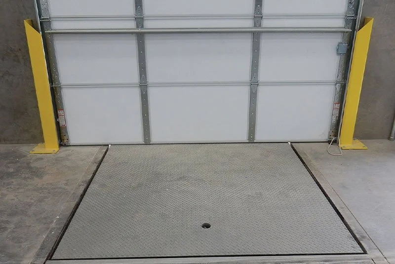 Industrial garage door with yellow safety guards on each side and a removable ramp leading into the doorway.