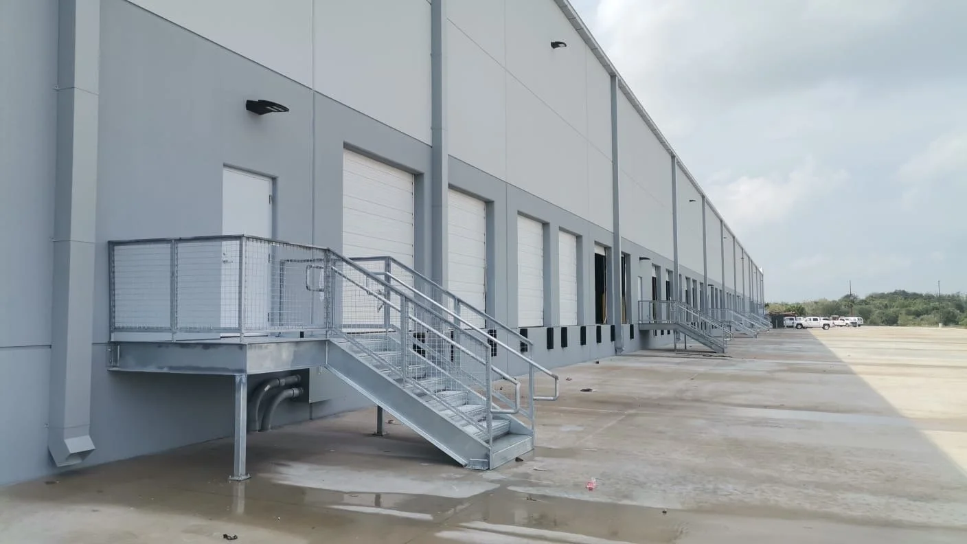 Exterior of a large warehouse with multiple loading dock doors and metal stairs.
