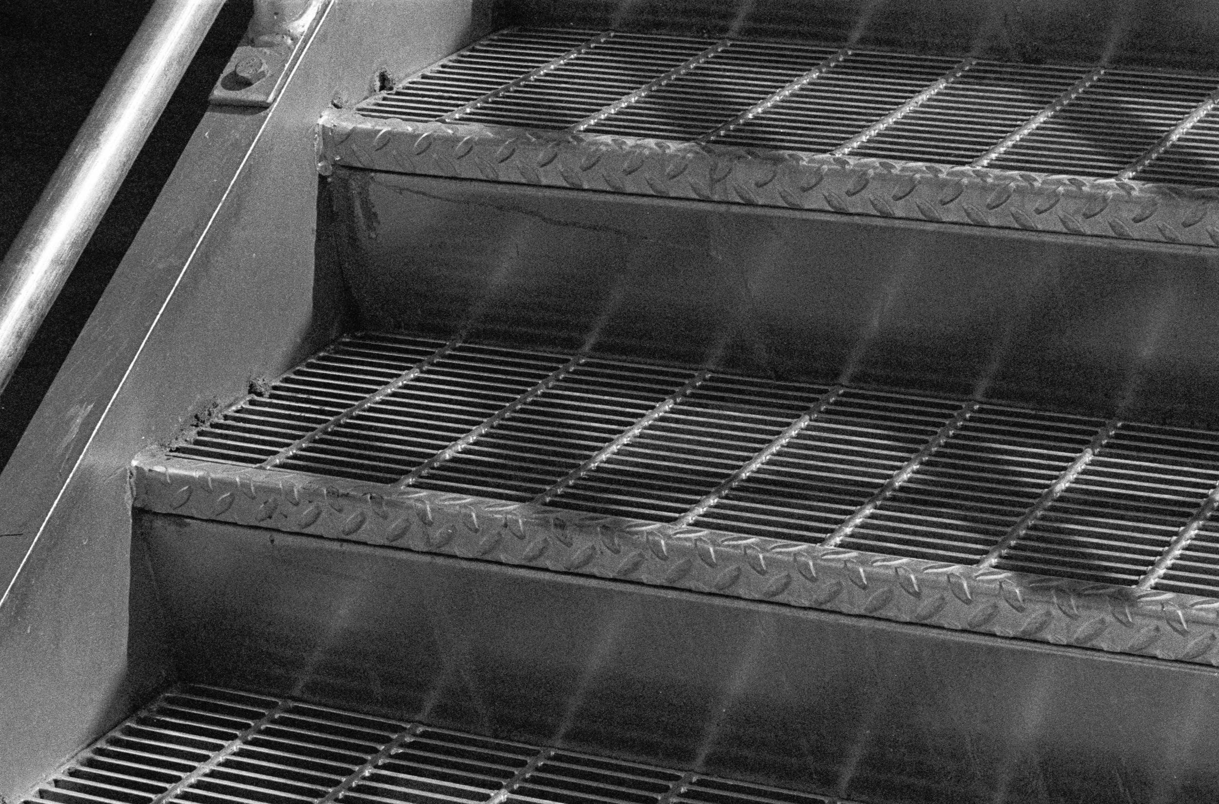 A black and white photo of a metal staircase with grated steps and diamond plate edges.