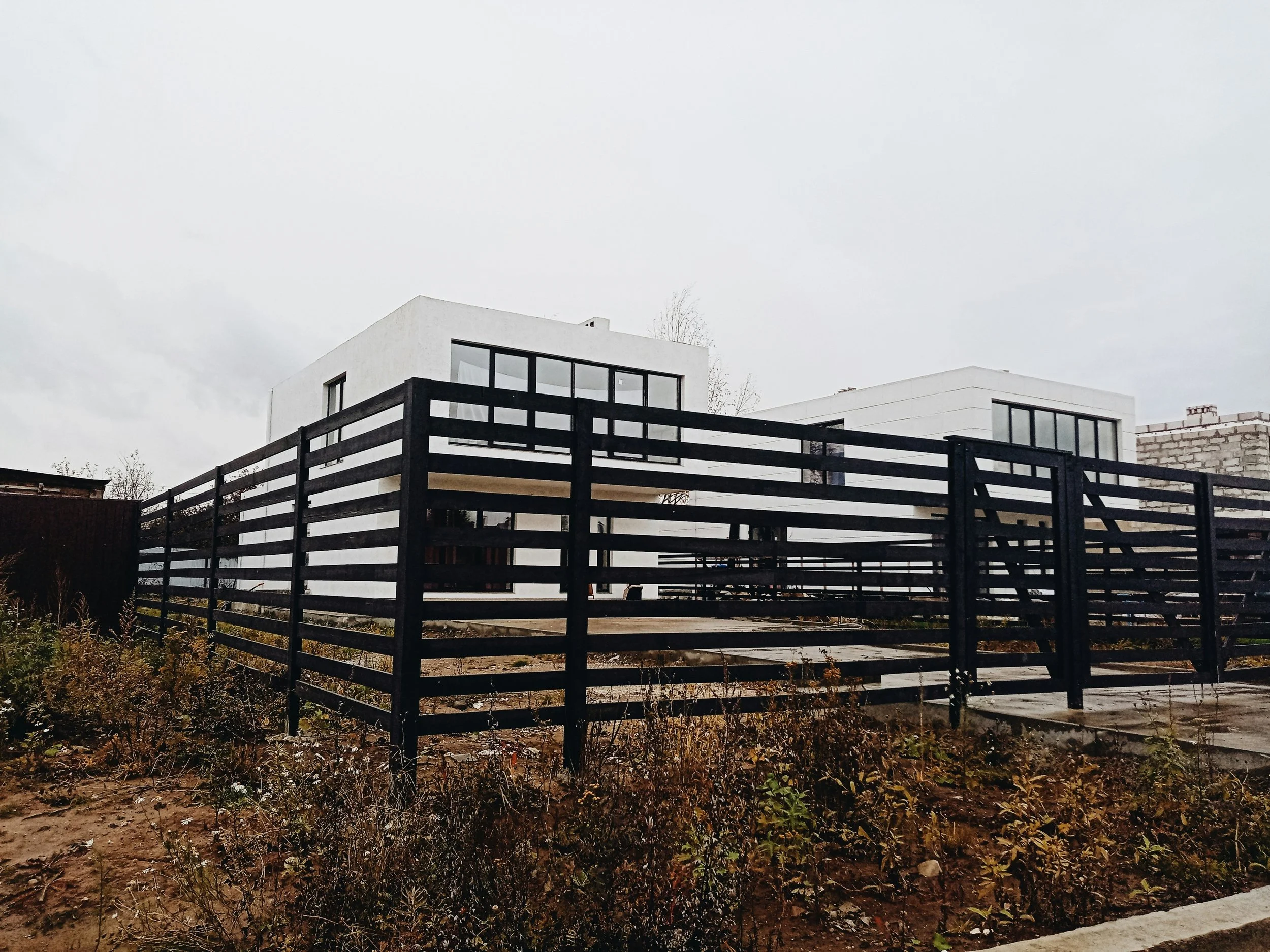 Modern white residential building with large windows and black fencing in front, overcast sky.