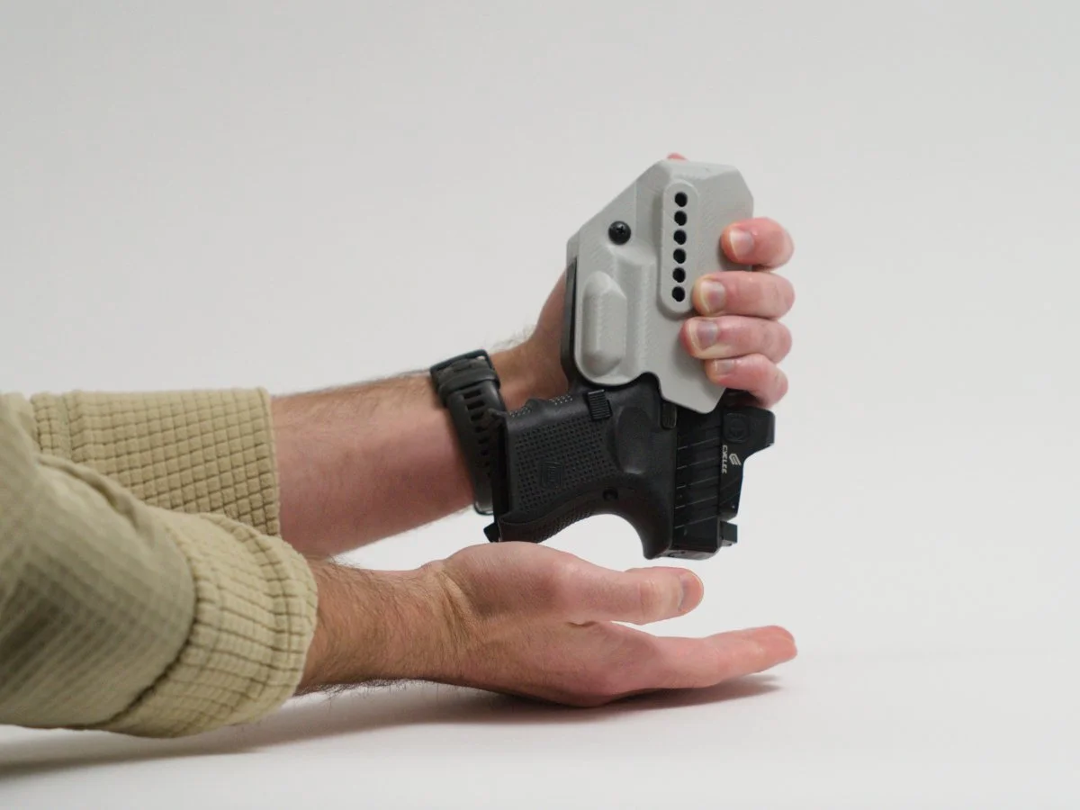 A person checking the retention on a gray Mockingbird Holsters holster by holding the holstered Glock firearm upside down in one hand, and attempting to shake the firearm out of the holster into their opposite hand.