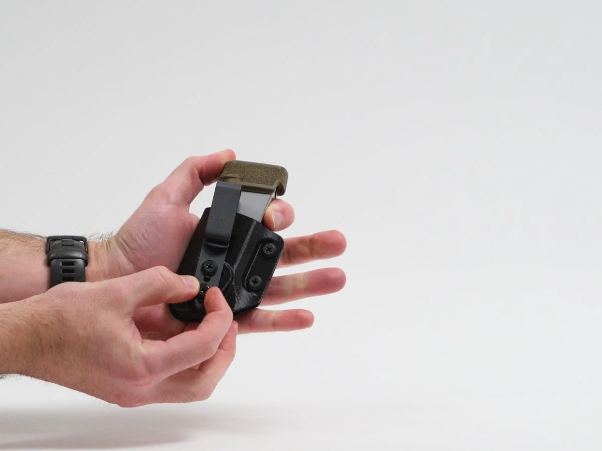 Person checking the tightness of the screws holding a belt clip on a black Mockingbird Holsters magazine pouch containing a Springfield Armory Hellcat magazine.