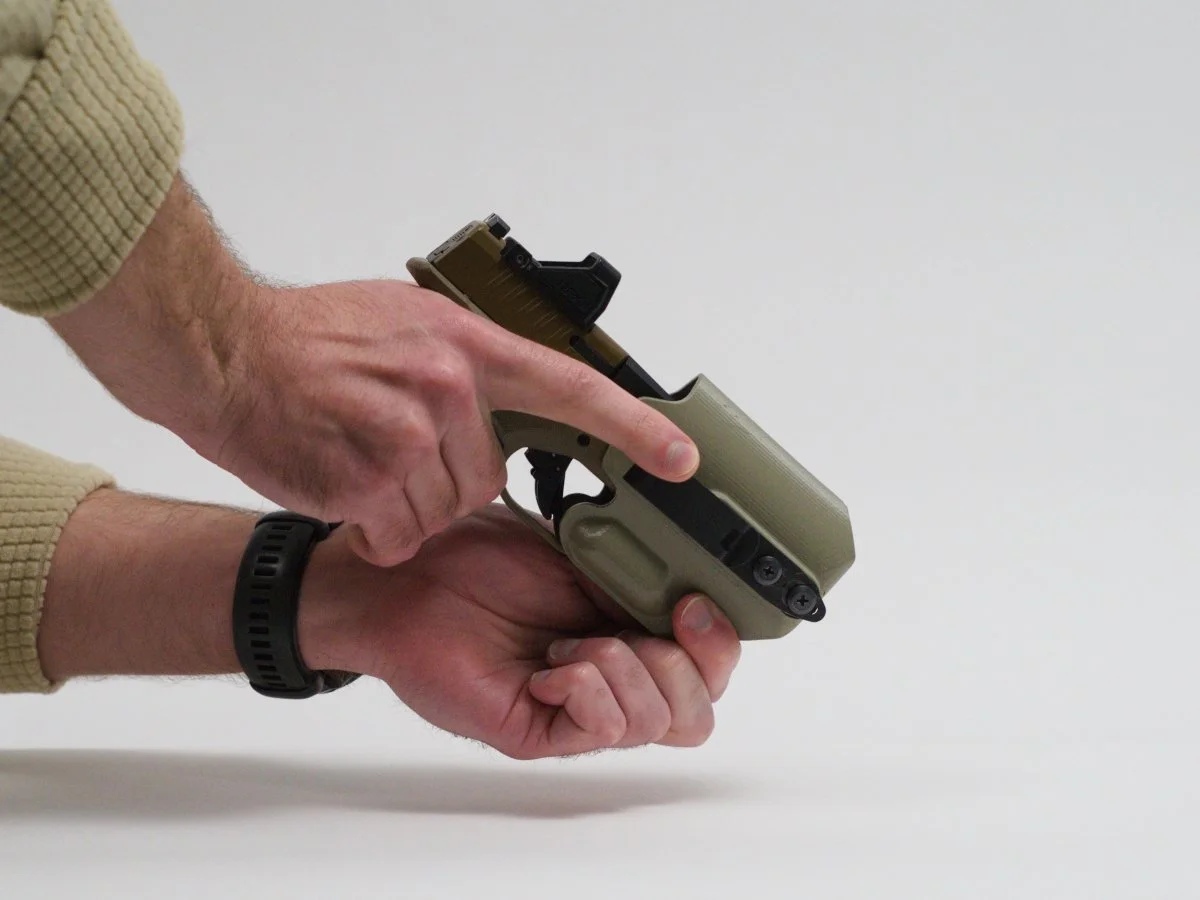 A person inserting a Springfield Armory Hellcat handgun into a foliage green Mockingbird Holsters holster, keeping their fingers out of the way of the muzzle.