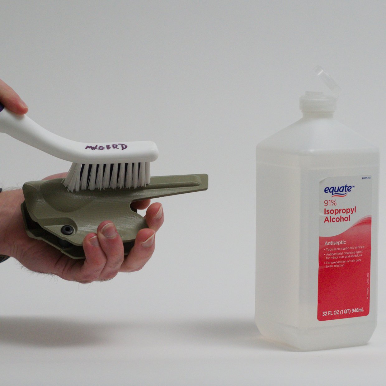 Person cleaning a foliage green Mockingbird Holsters holster with a white brush next to a bottle of 91% Isopropyl Alcohol against a plain white background.