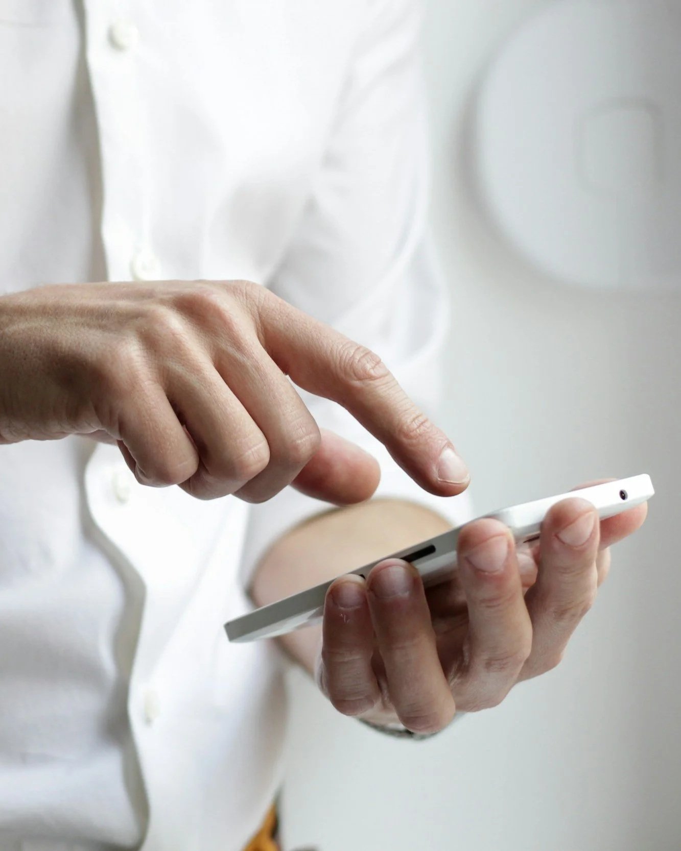 Close-up of a person in a white shirt using a smartphone, with focus on their hands and the device.