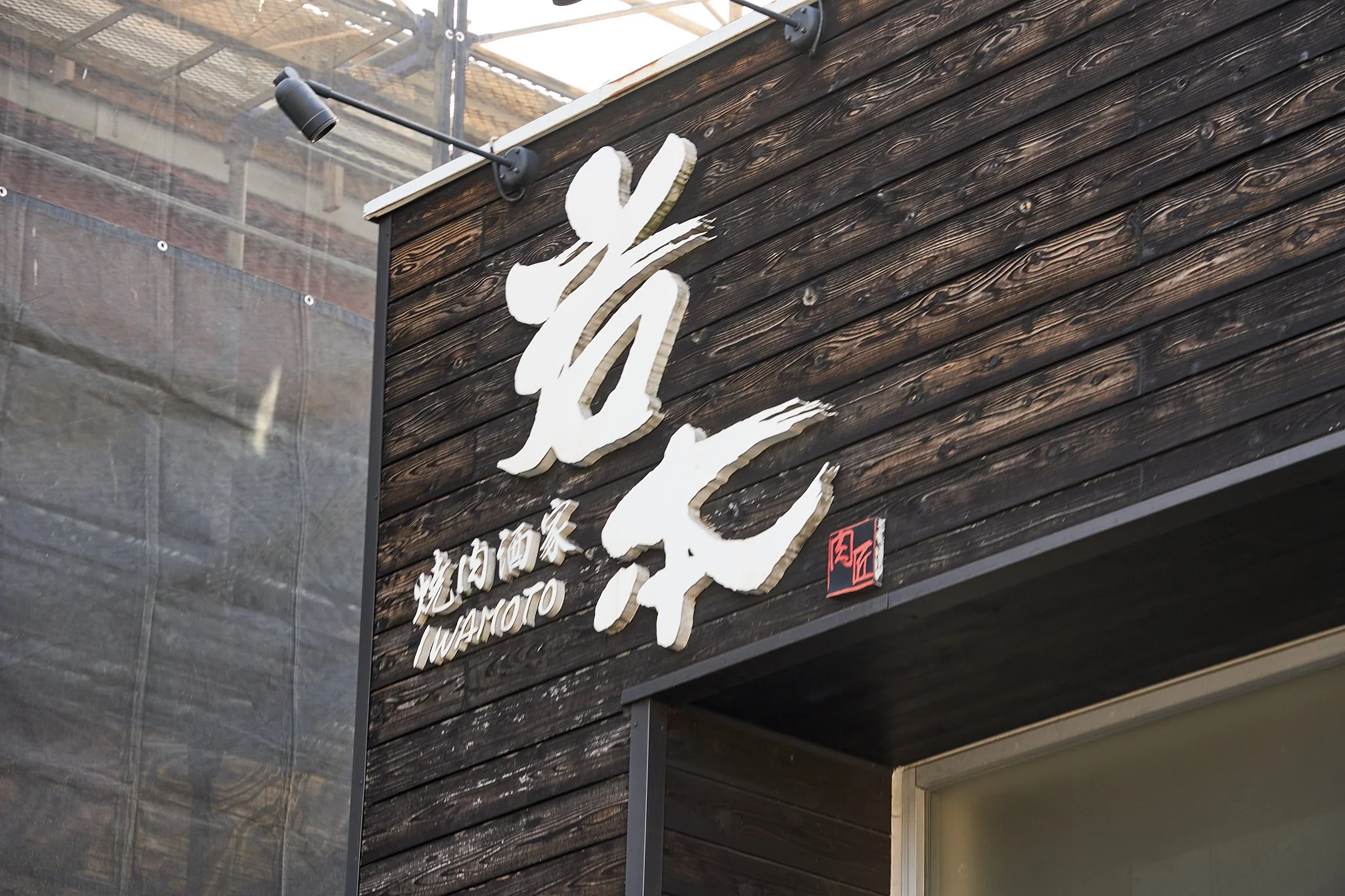 黒い木の壁に白い文字で「焼肉居酒屋」と書かれ、その下に「IWAMOTO」と書かれている看板。