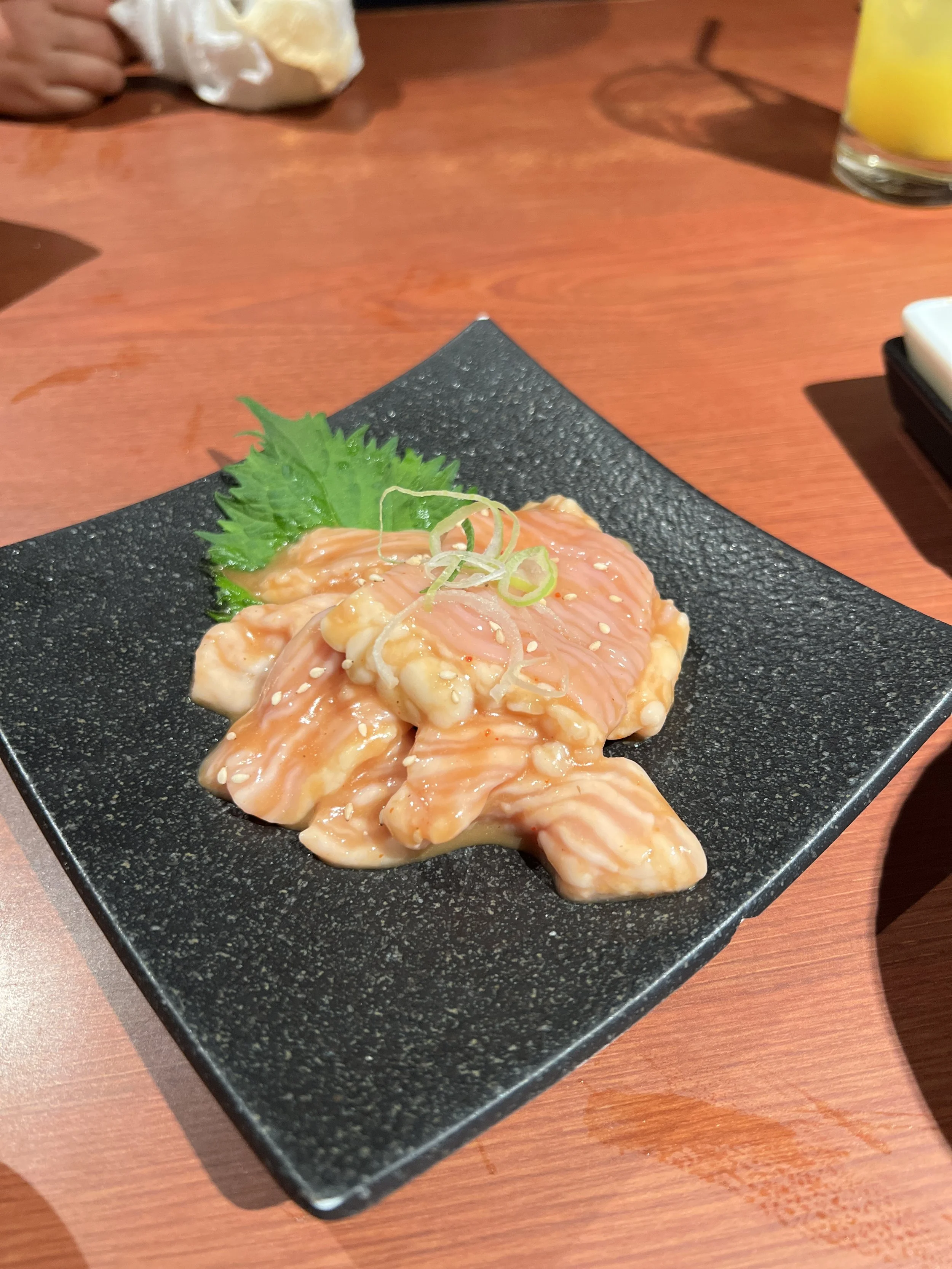 皿に盛られた生の鶏肉とネギのスライス。緑のシソの葉も添えられている。