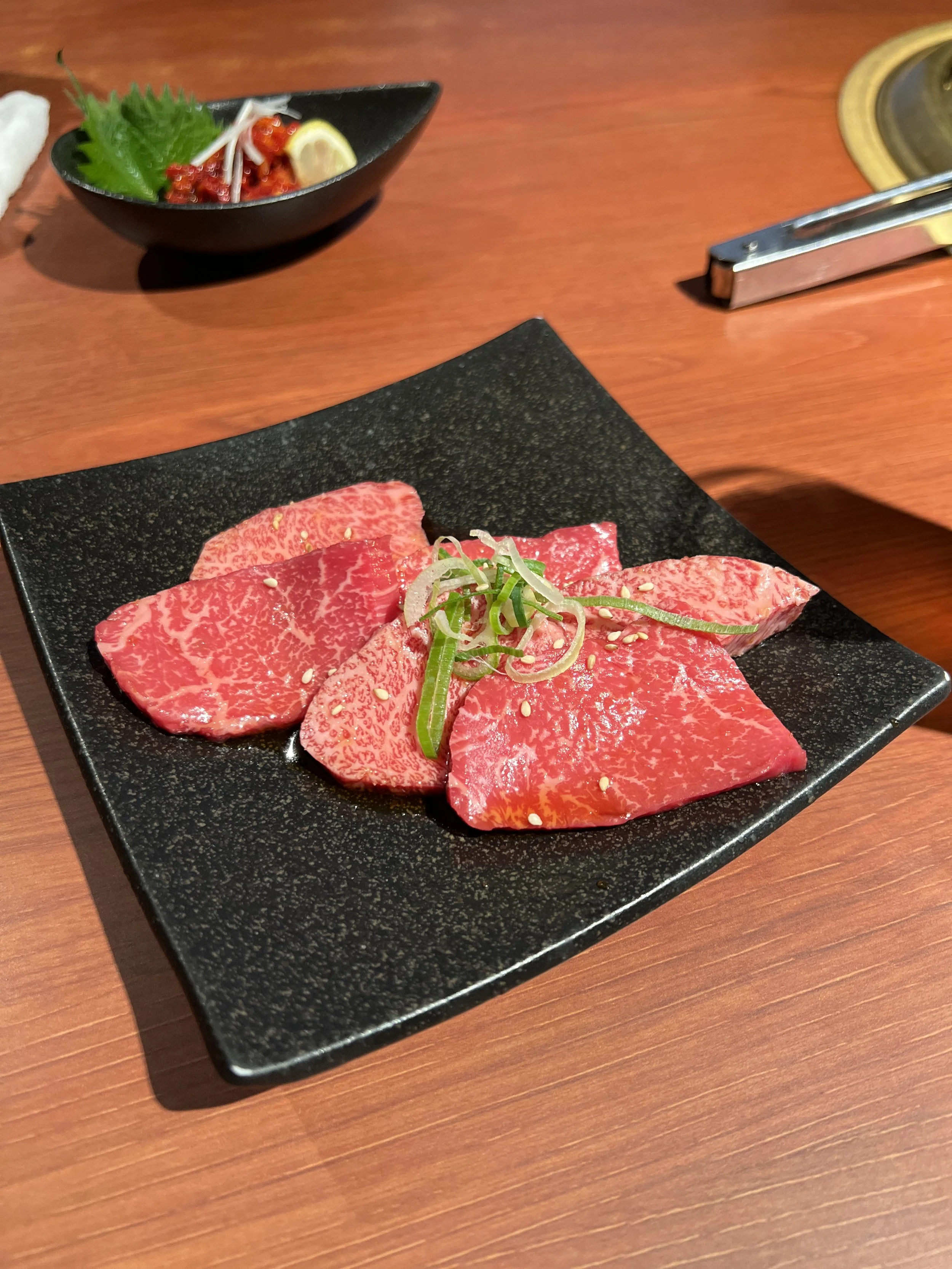 サシの入った牛肉の刺身と小ネギのトッピングが乗った黒い長方形の皿