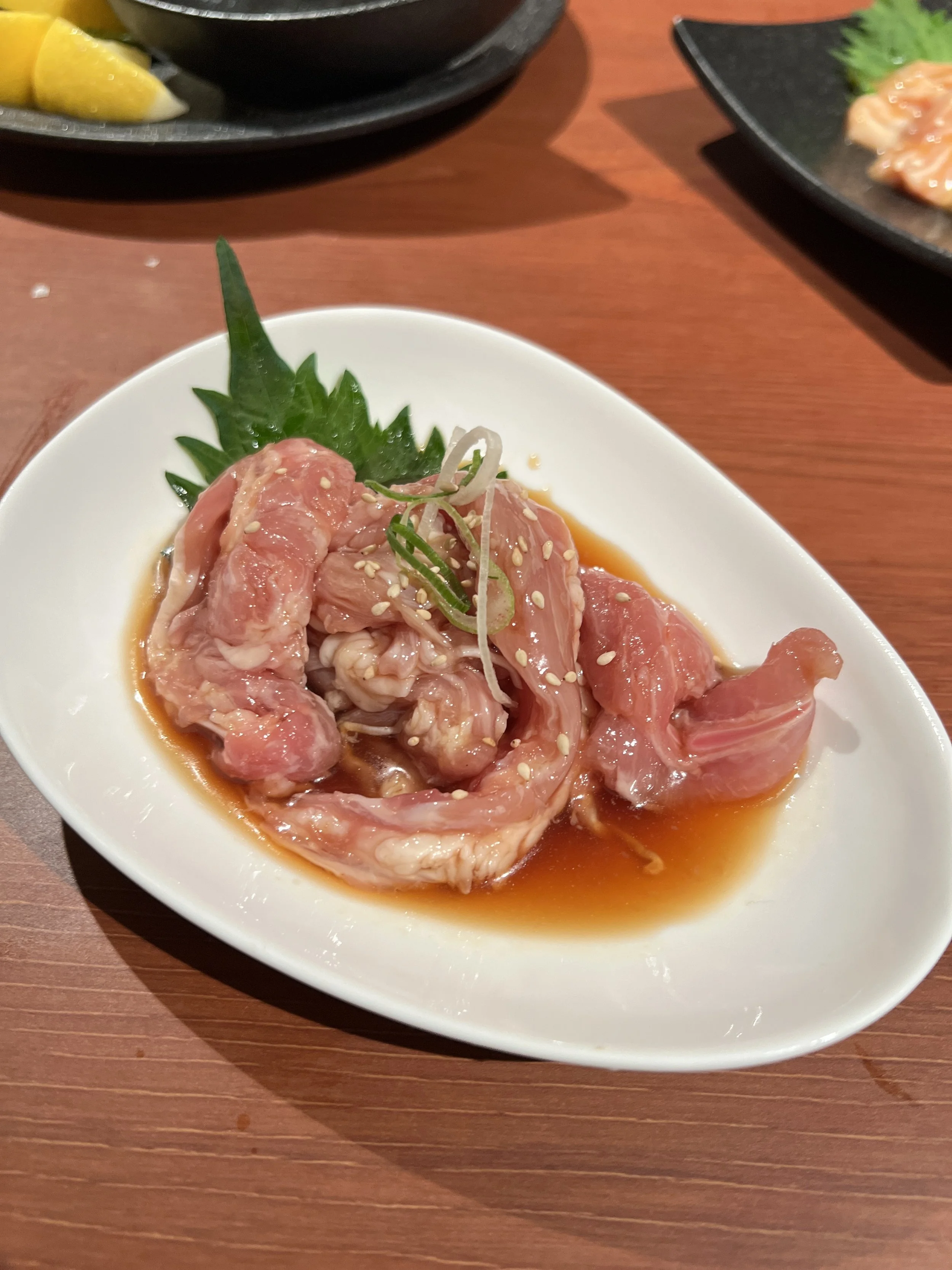 皿に盛られた生の鳥肉と刻んだネギ、ゴマがのっている刺身料理。