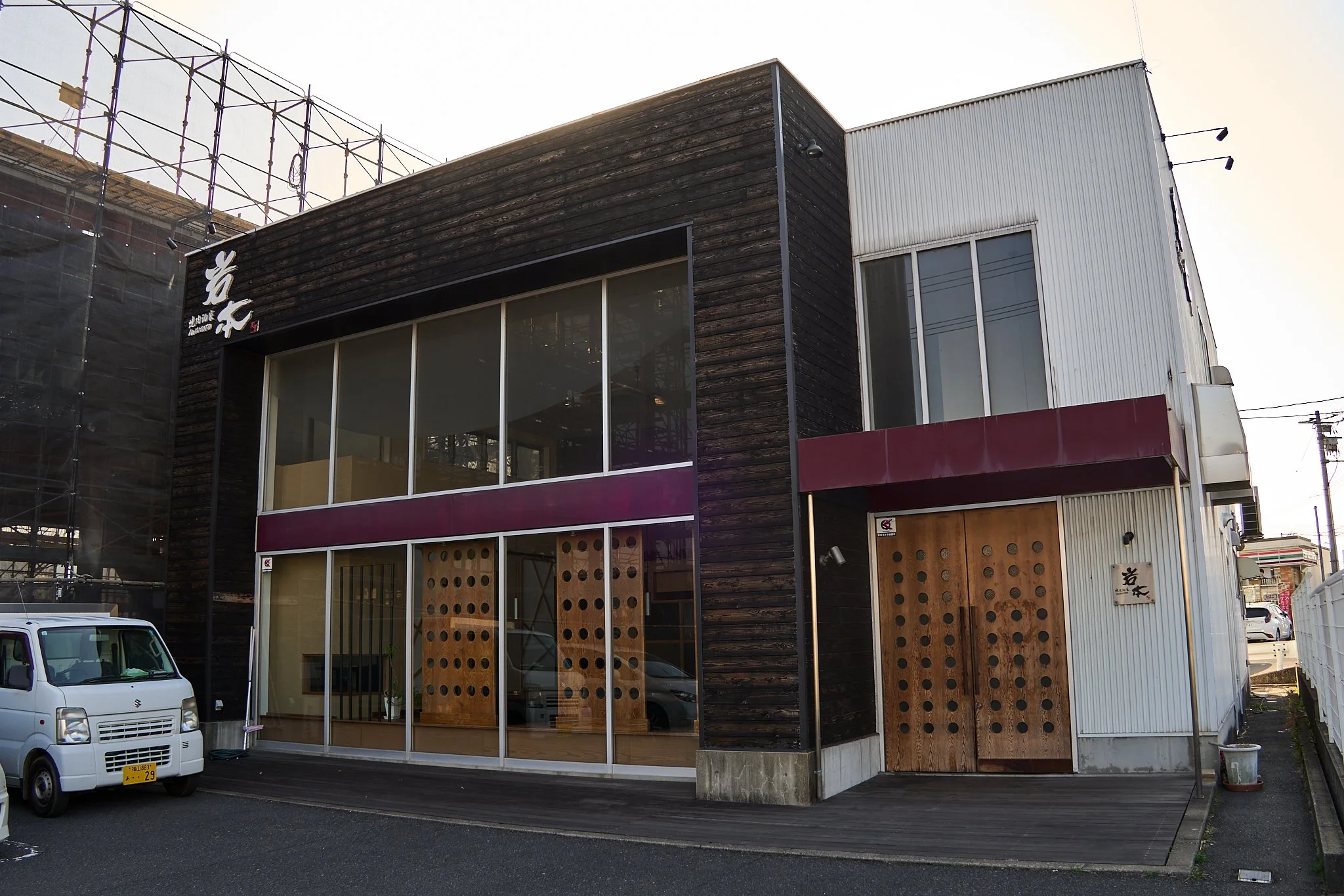 木製の外壁と大きなガラス窓が特徴のレストランの建物。入口には木製のドアと看板。駐車場に白い車が停まっている。