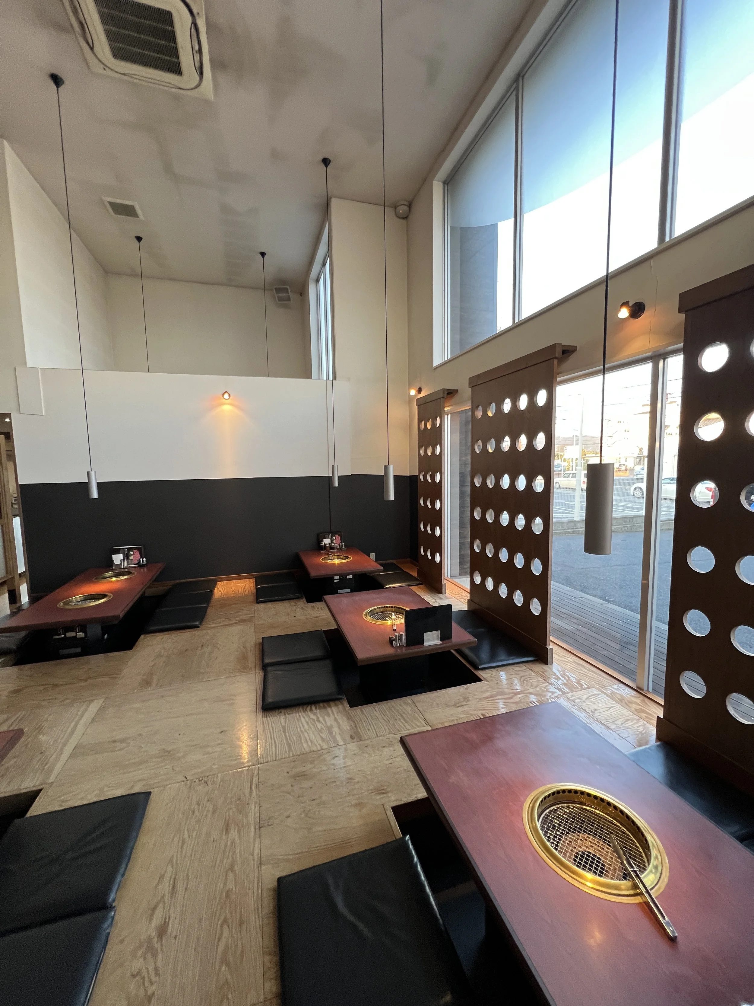 ニコニコのあるレストランの interior with low tables, cushions, and partition screens, large windows letting in natural light