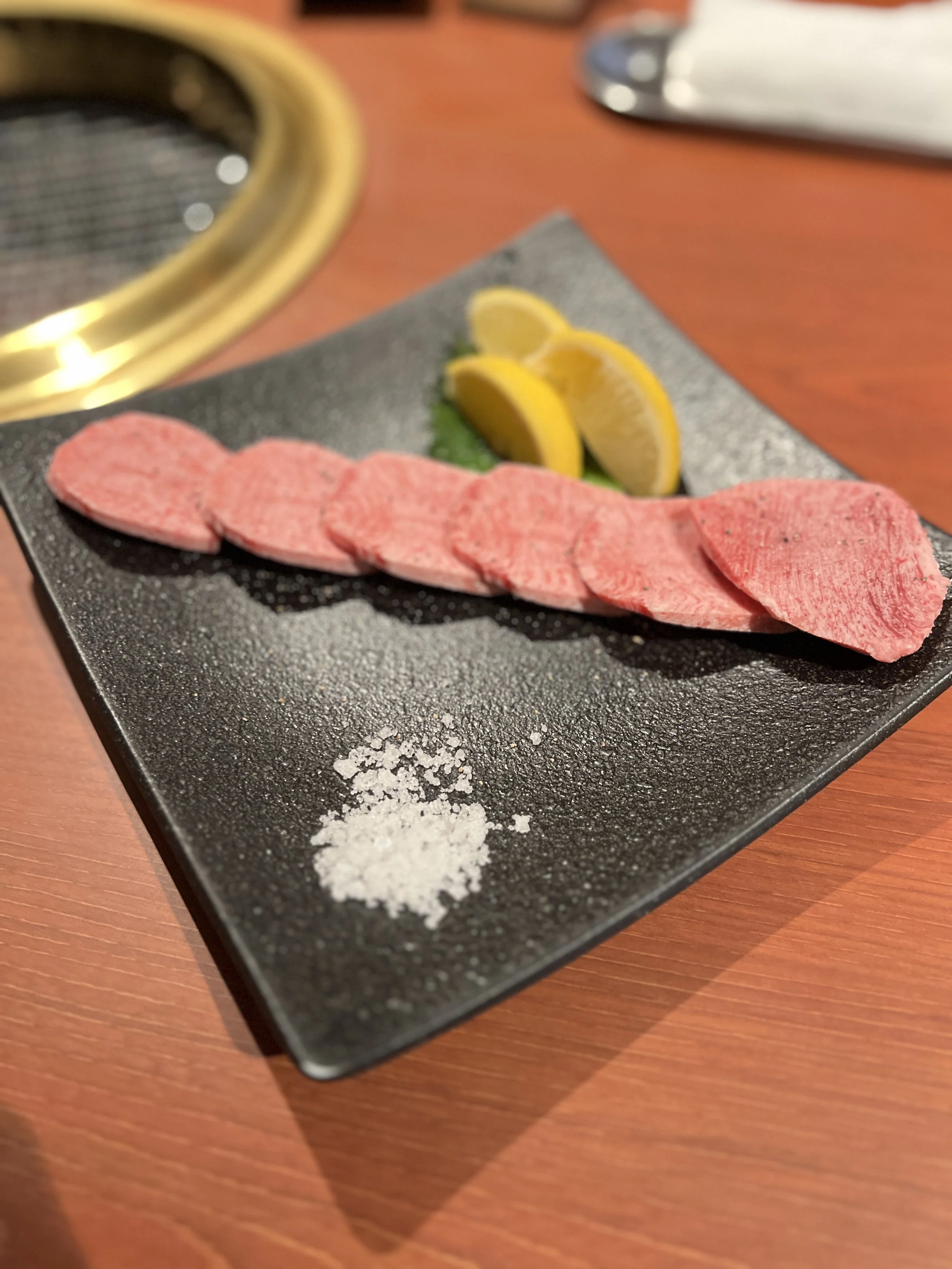 薄切りの肉とレモンの輪切りが盛り付けられた黒い皿