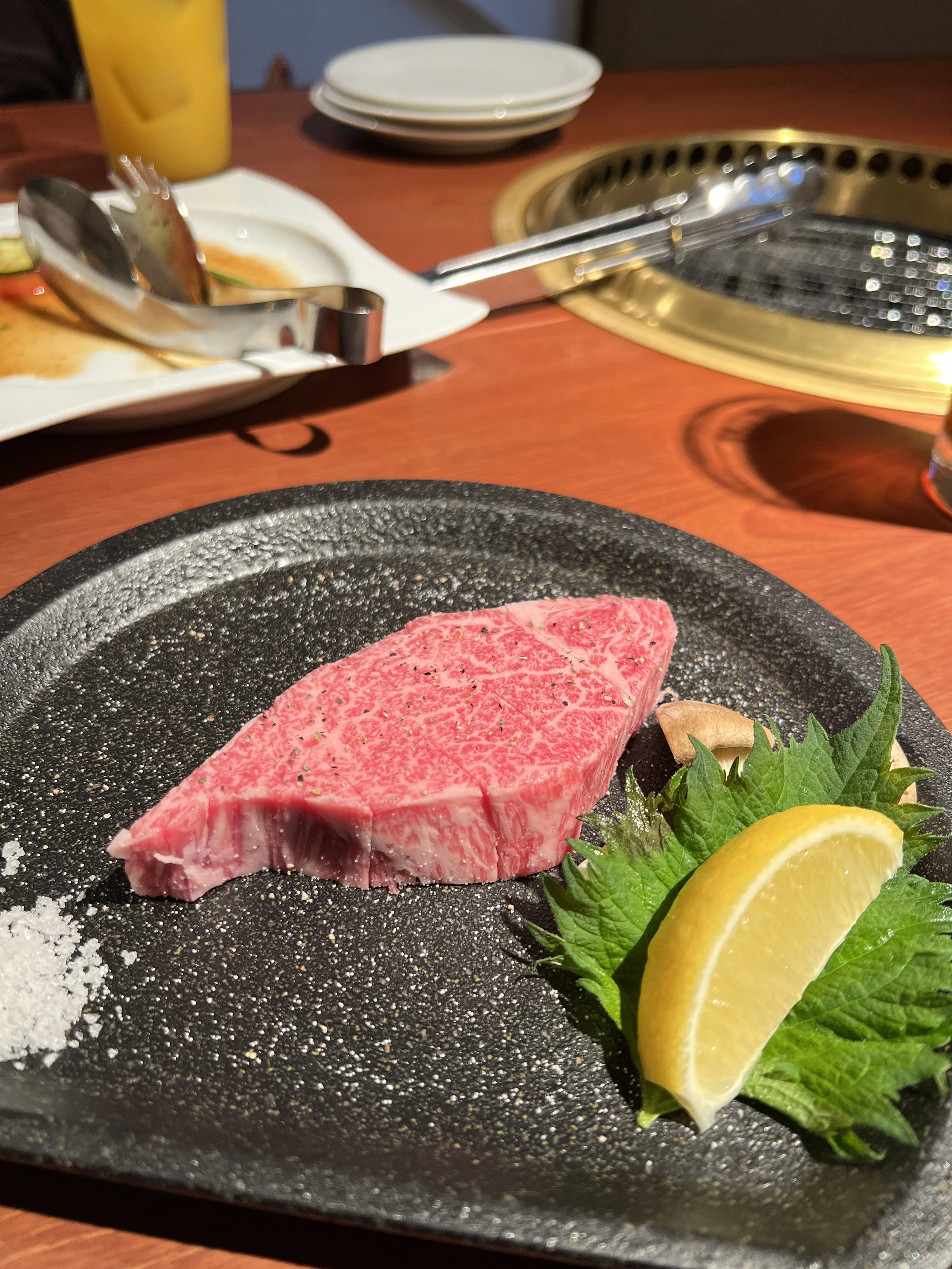 薄くて脂の乗ったステーキ肉とレモンのスライス、ハーブが盛り付けられた黒い皿。