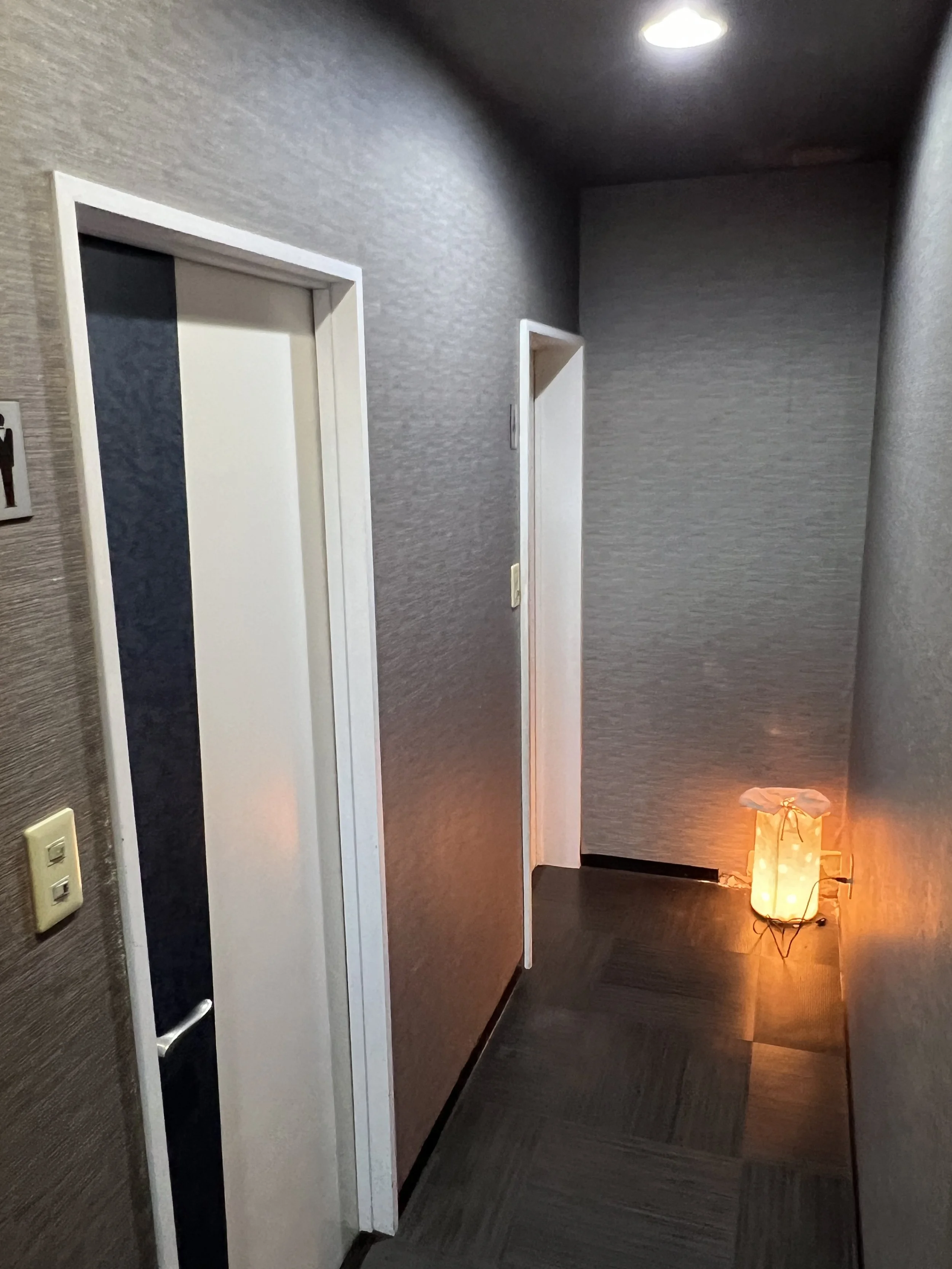 廊下の片側には扉があり、壁の隅に暖色系のランプが置かれている