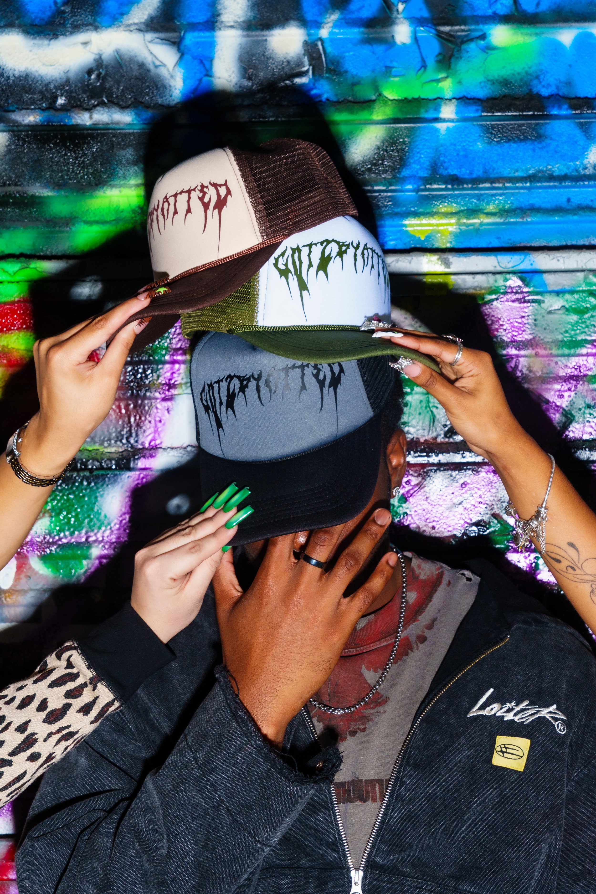 Person holding three trucker caps with graffiti background