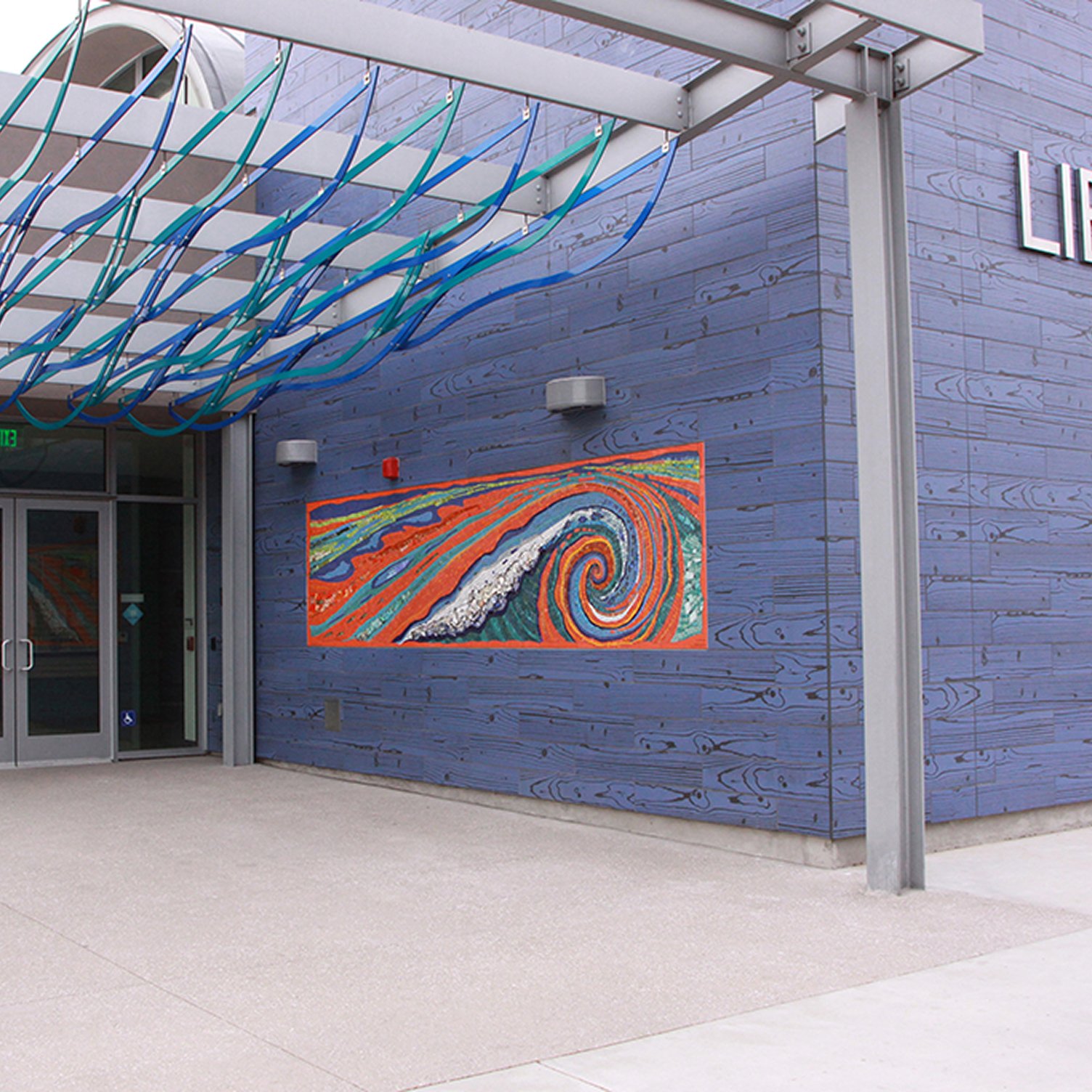 Exterior of a modern building with blue wood siding, colorful spiral artwork on the wall, and a glass entrance door.