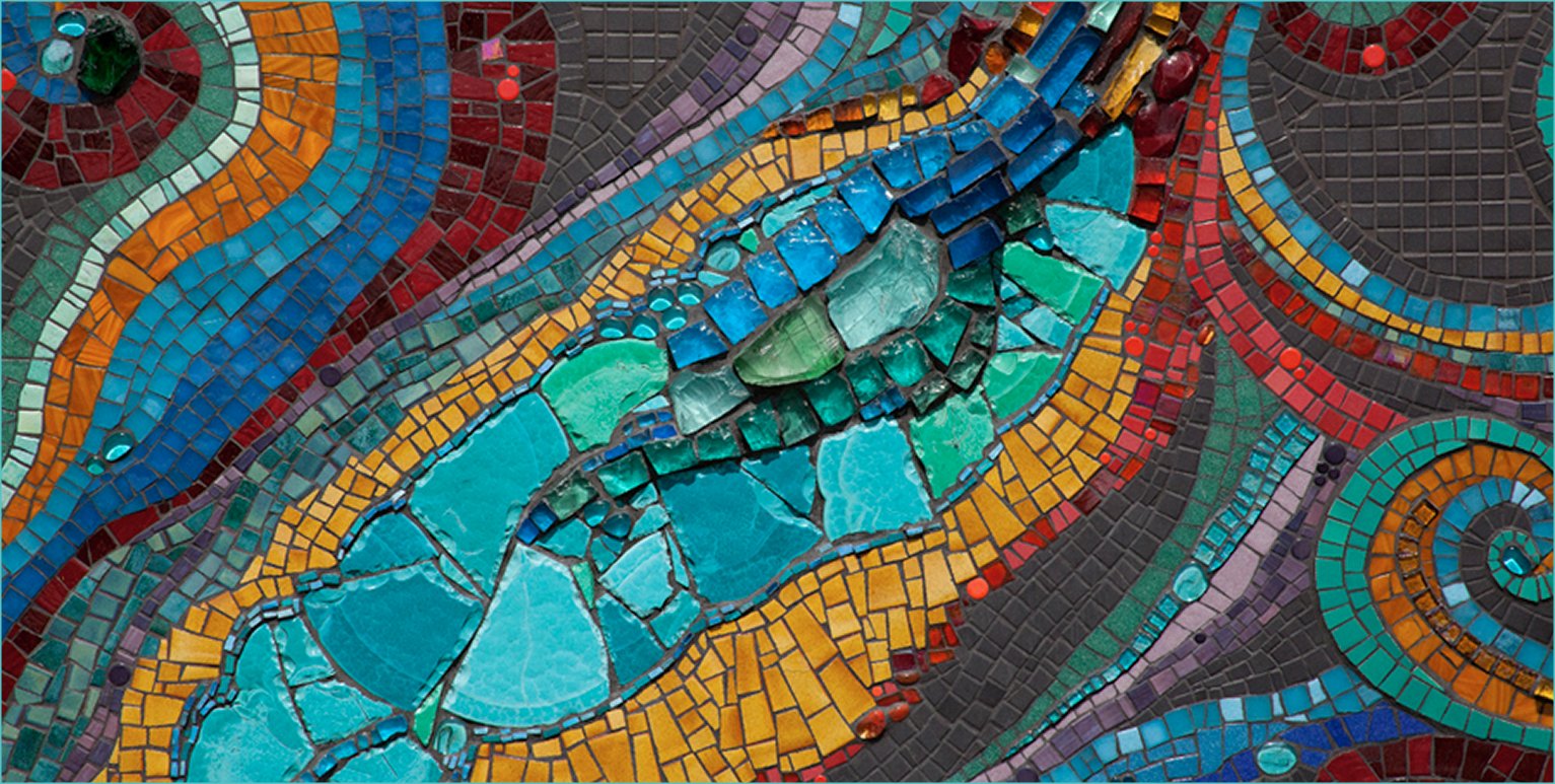 Close-up of a colorful mosaic with swirling patterns, made of small, irregularly shaped tiles in shades of blue, green, red, orange, and purple.