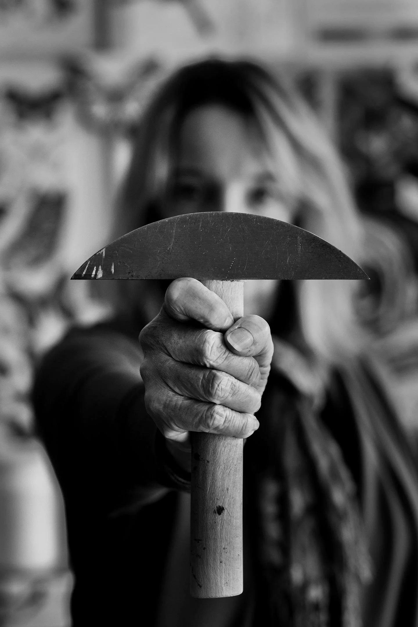 Close-up of an elderly person's hand gripping a wooden stick, with the person's face blurred in the background.