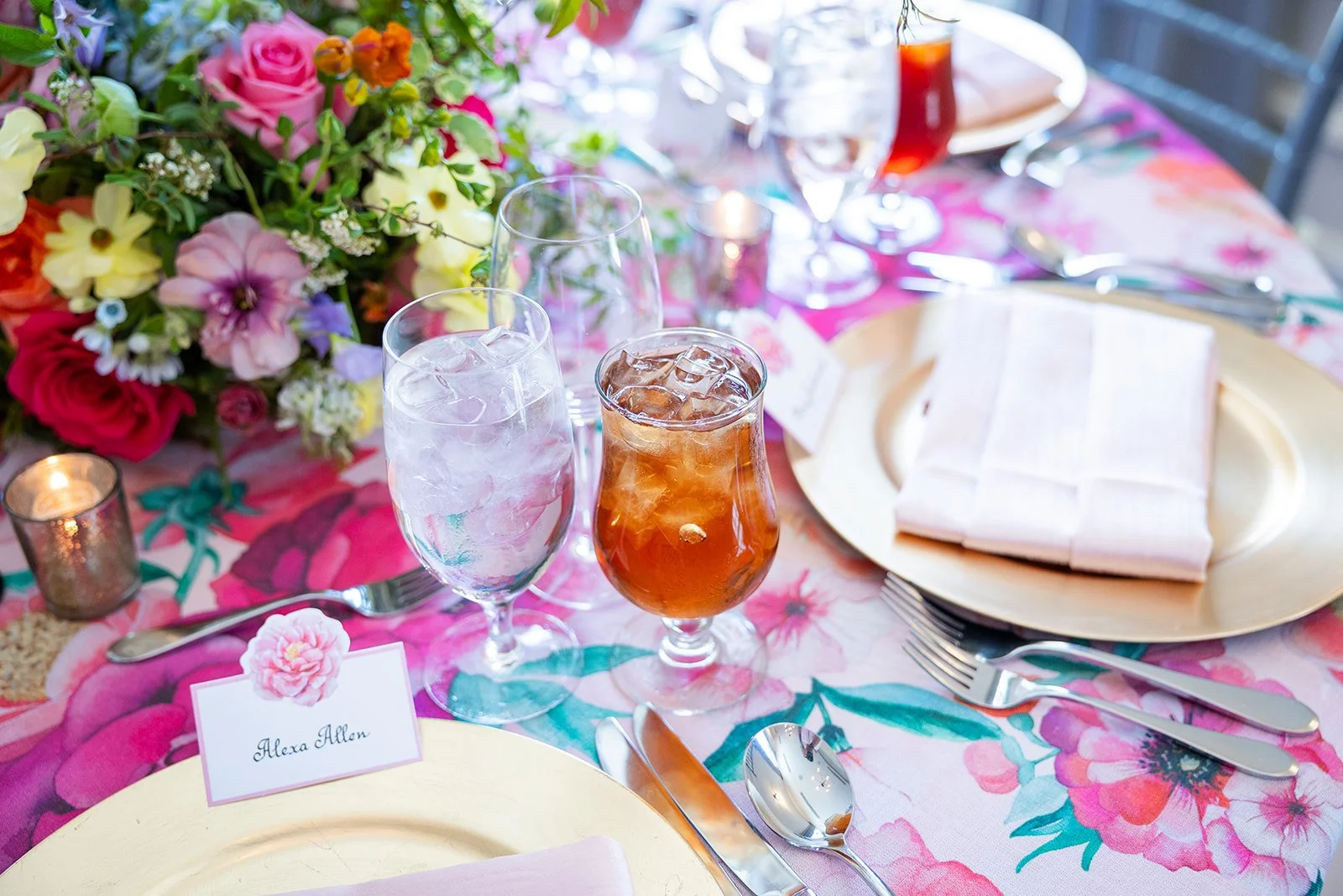 Close-up of floral print tablecloth table setting with gold charger plate and personalized place card at Morrison House