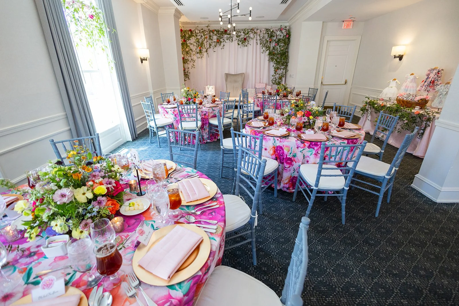 Wide angle view of fully decorated Morrison House ballroom featuring floral tablecloths, blue chiavari chairs, and cascading floral wall installation