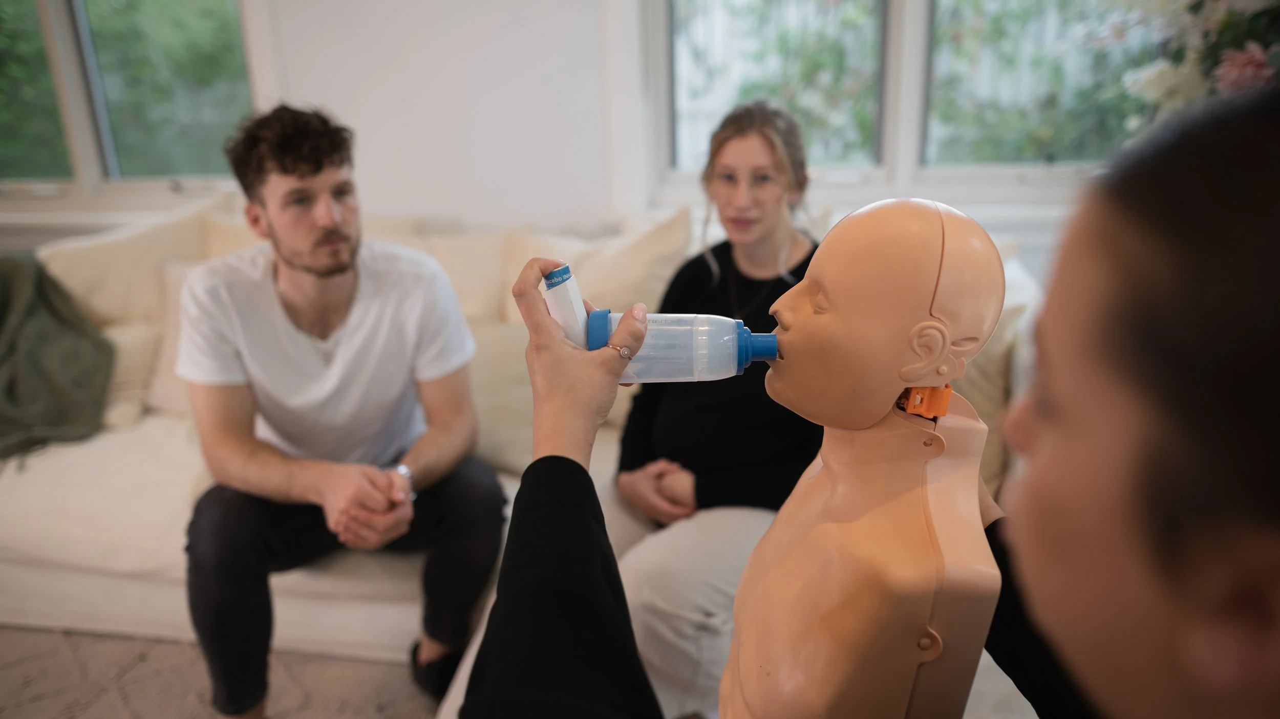 Person practicing rescue breathing on a medical training mannequin while others observe.