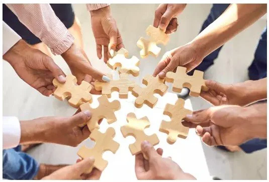 Multiple hands assembling wooden puzzle pieces on a table.