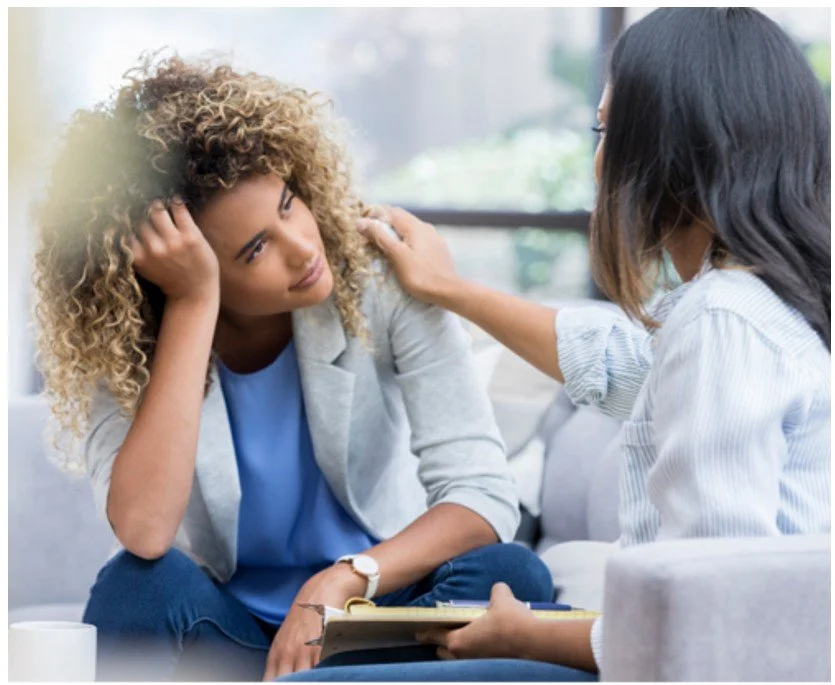 A woman appears to be distressed and leaning on her hand during a conversation with a counselor or therapist in a therapy session.