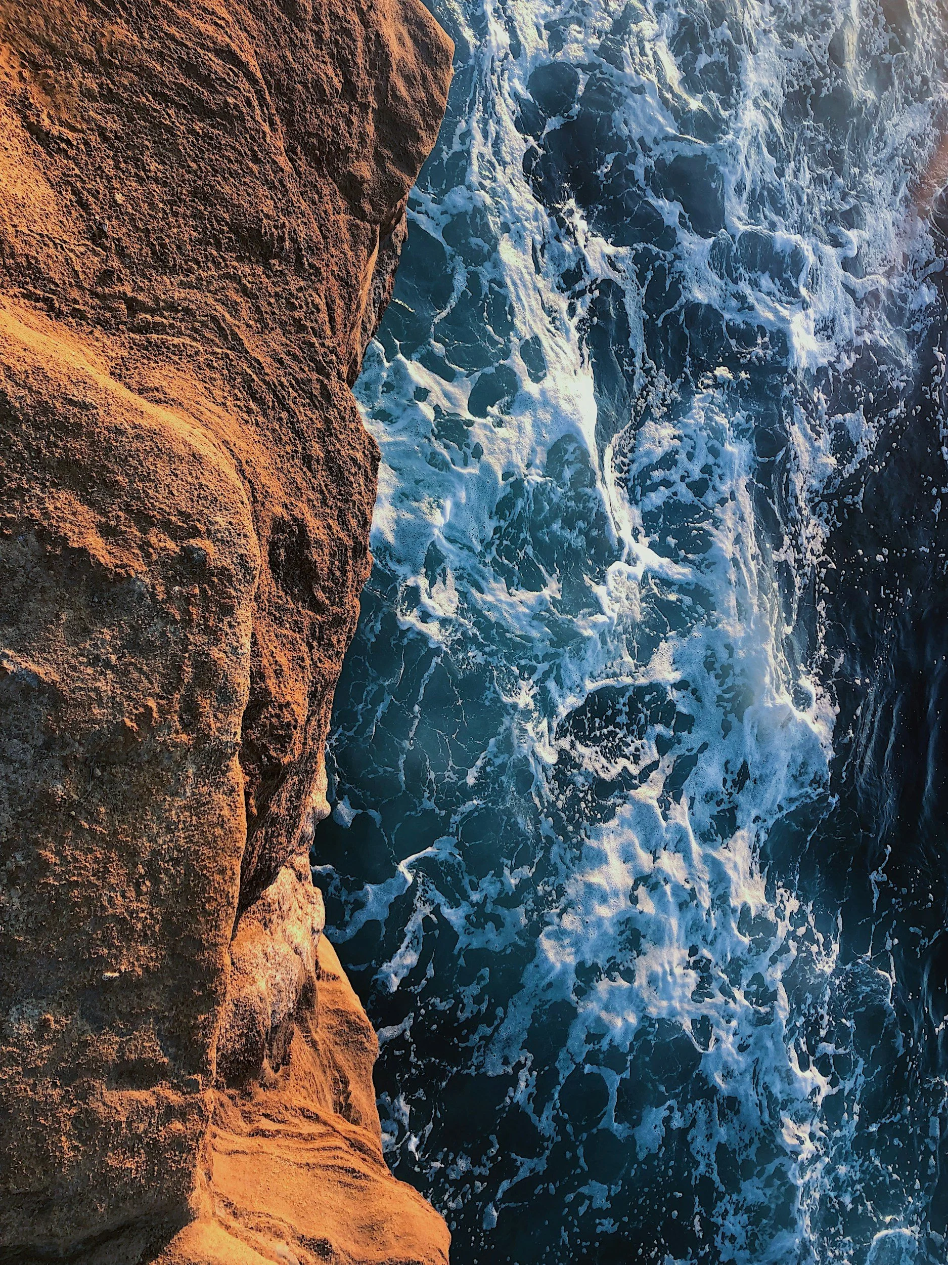Close-up of a rocky cliff with water crashing against it, creating white foam and waves.