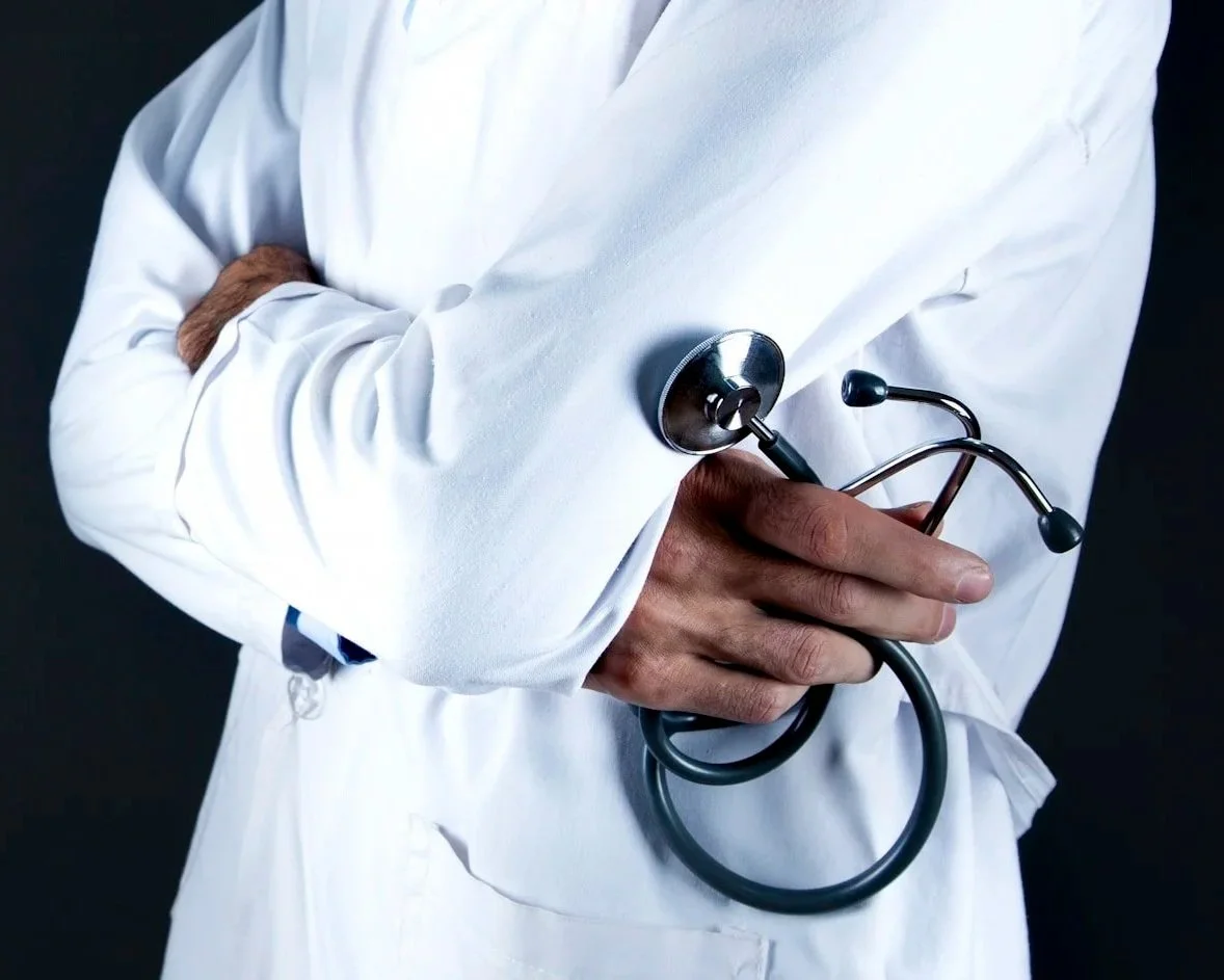 A doctor in a white coat holding a stethoscope against a dark background.