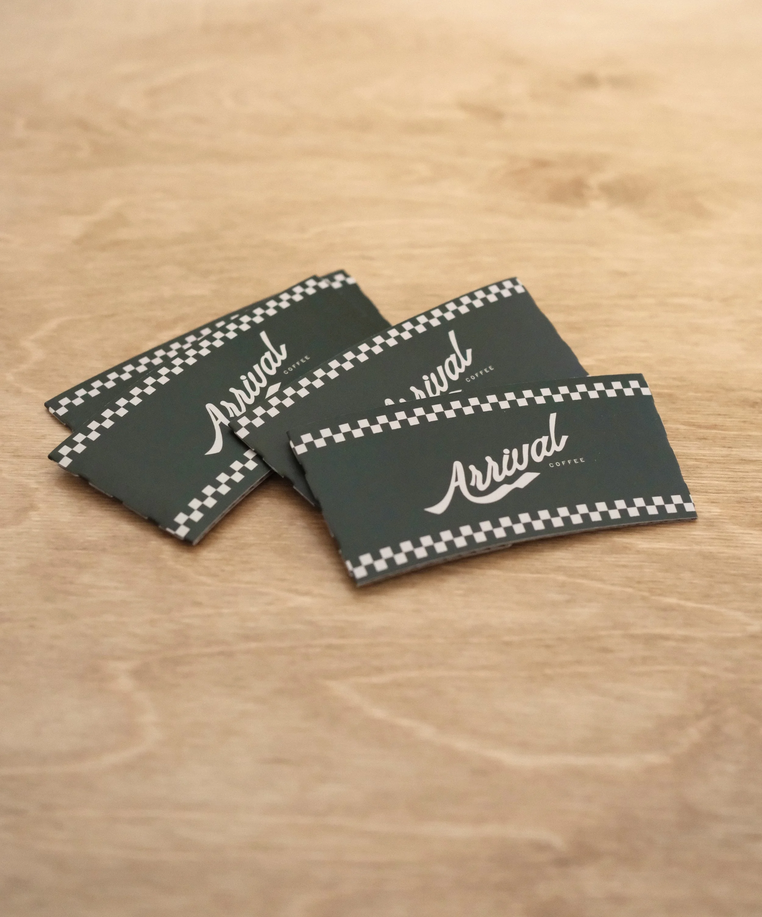 Multiple black and white checkered cards with the word 'Arrival' written in cursive white text on black background, placed on a wooden surface.