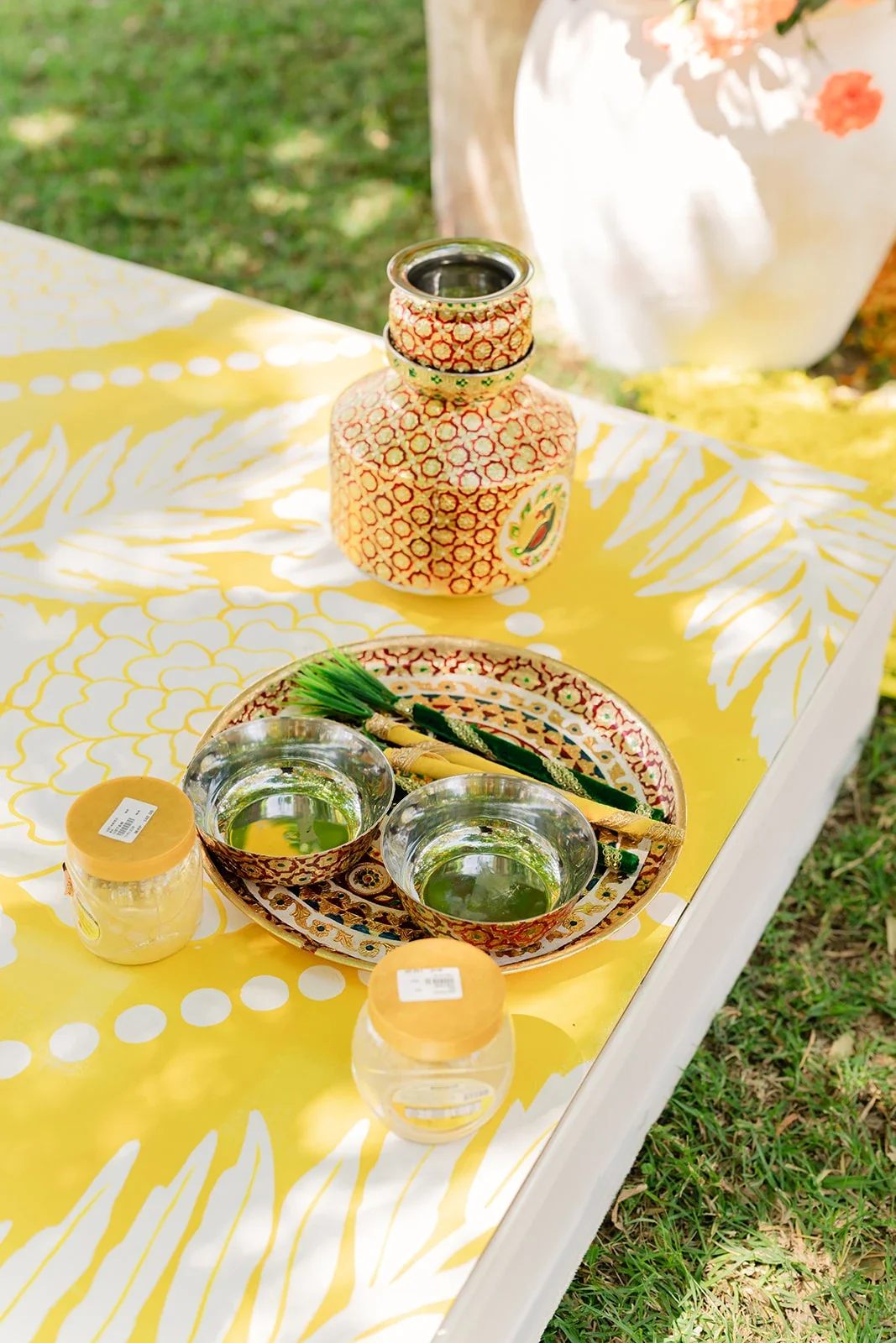 Decorative vase, bowls, and tableware on a yellow tablecloth outdoors.