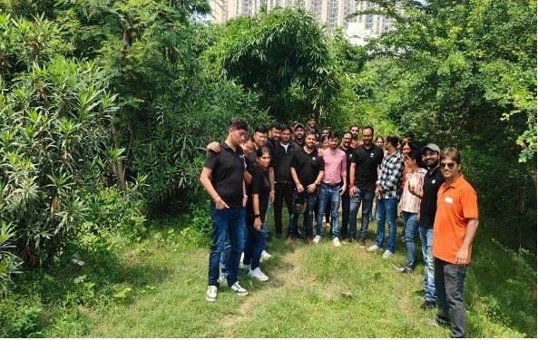 Group of people standing outdoors in a lush green park with trees and bushes.