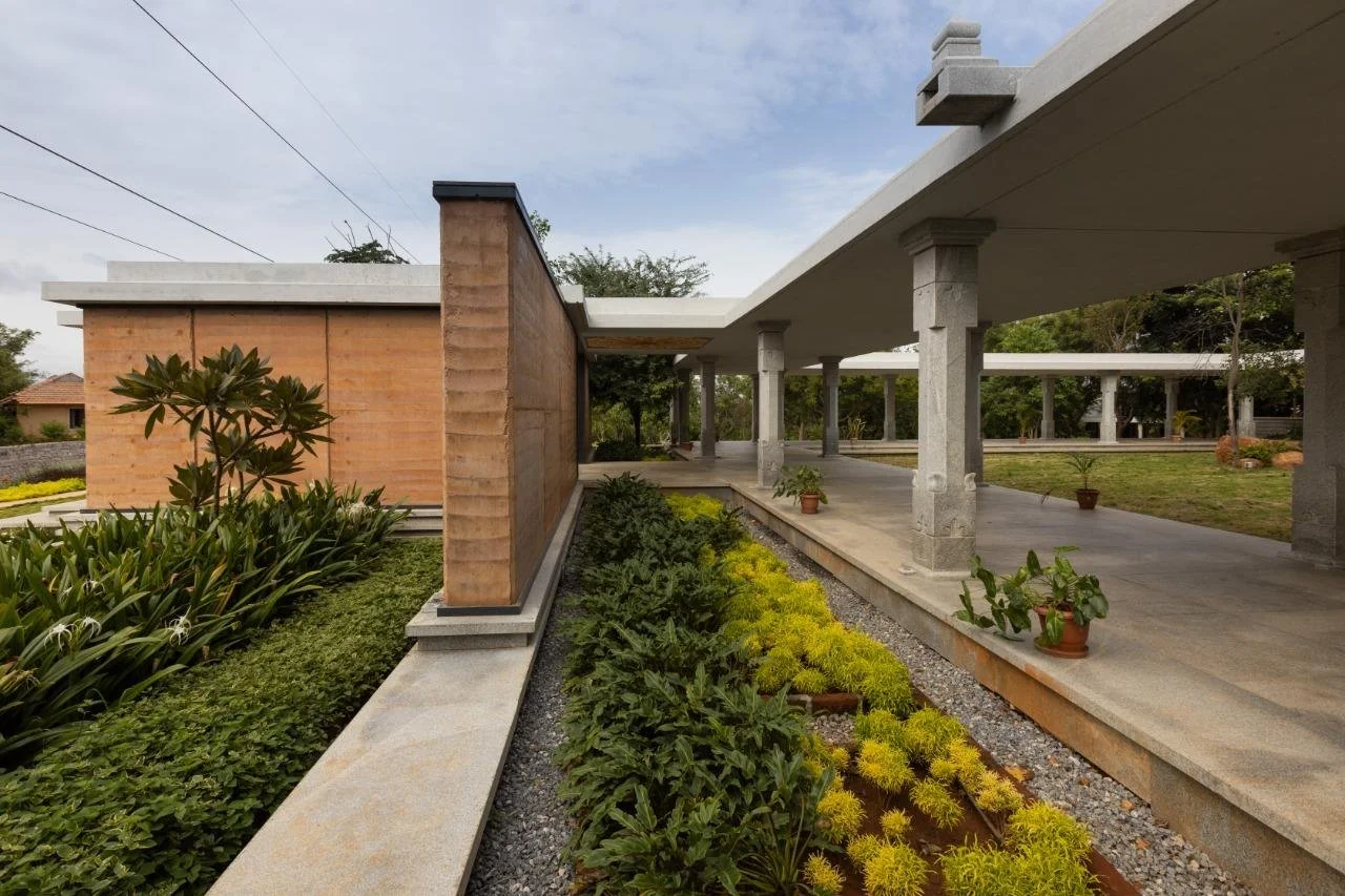 Modern house with open walkway, stone columns, and landscaped garden with potted plants and various shrubs.