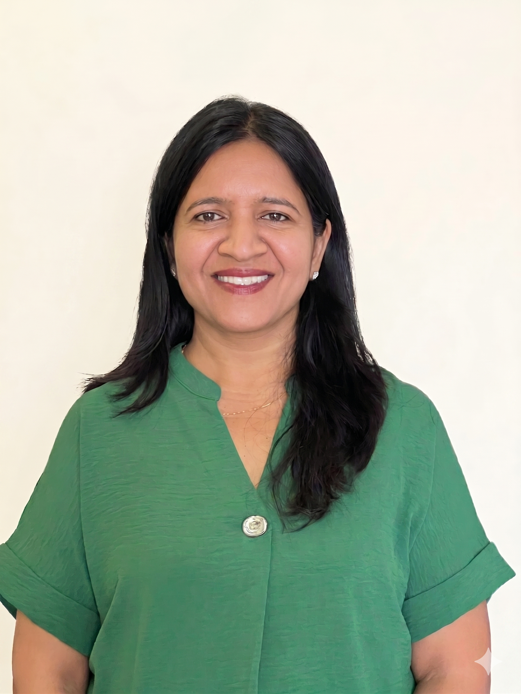 A woman with dark hair wearing a green top standing against a plain white wall.
