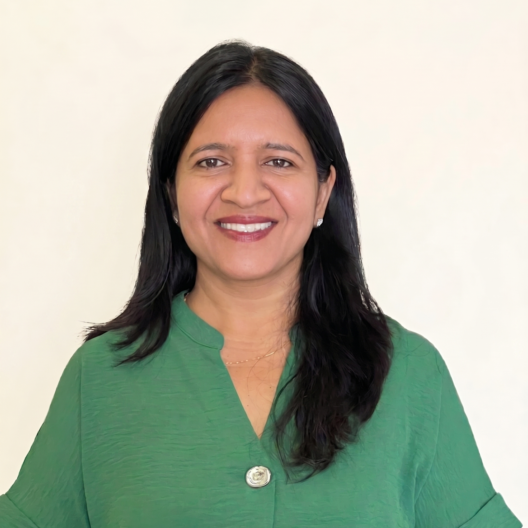 Close-up of a woman with dark hair wearing a green top and small earrings, smiling against a plain background.